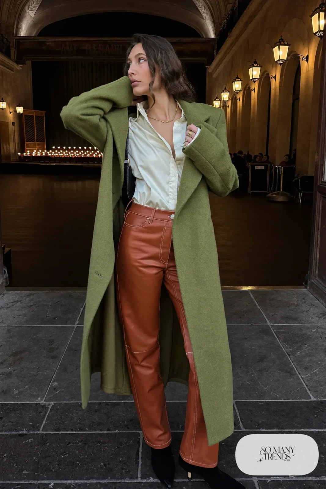 Woman in cognac faux leather straight pants, cream satin shirt, long moss green coat and black boots, outfit 14