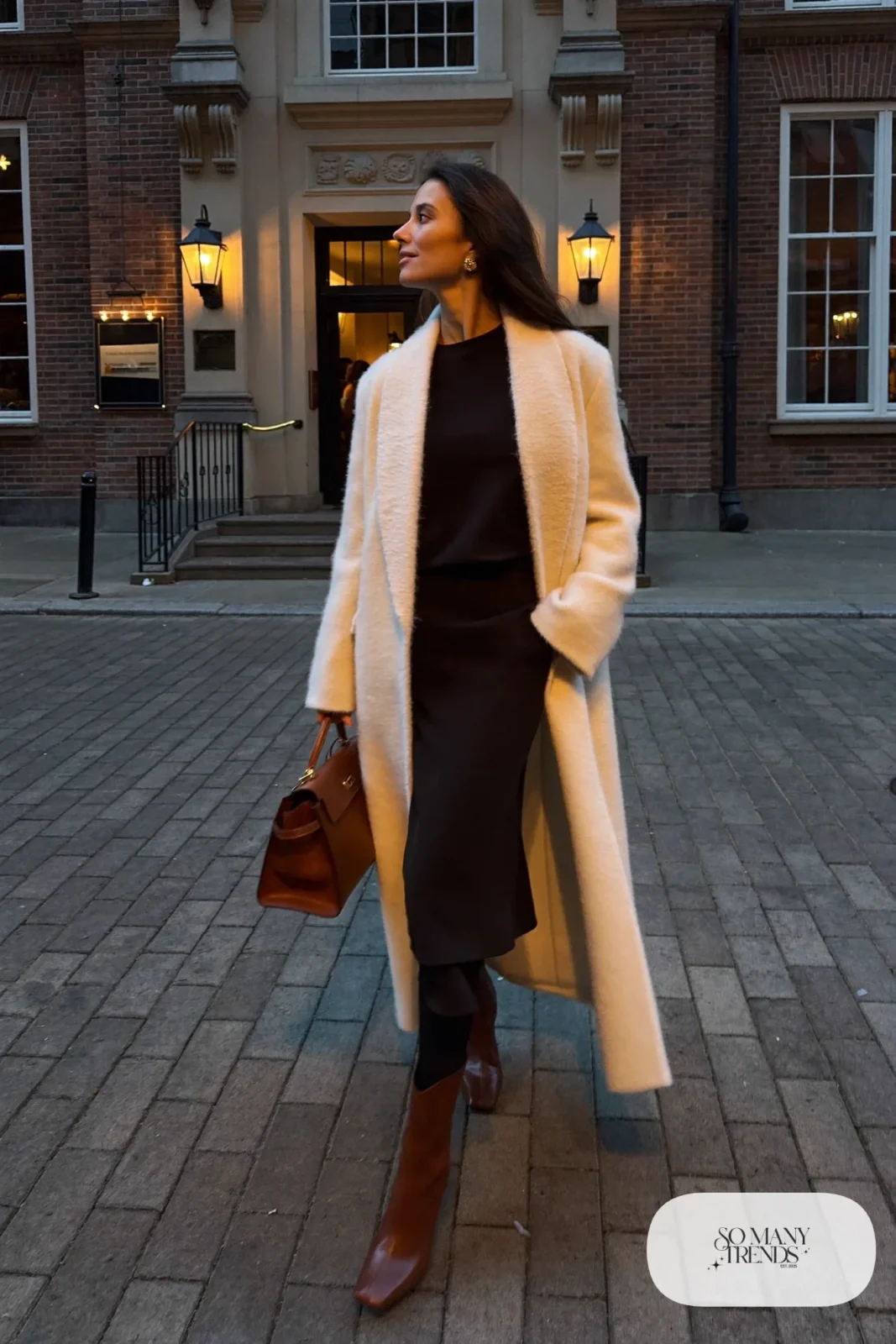 Woman in a long cream wool coat, black long sleeve midi dress, cognac boots and cognac bag, outfit 26