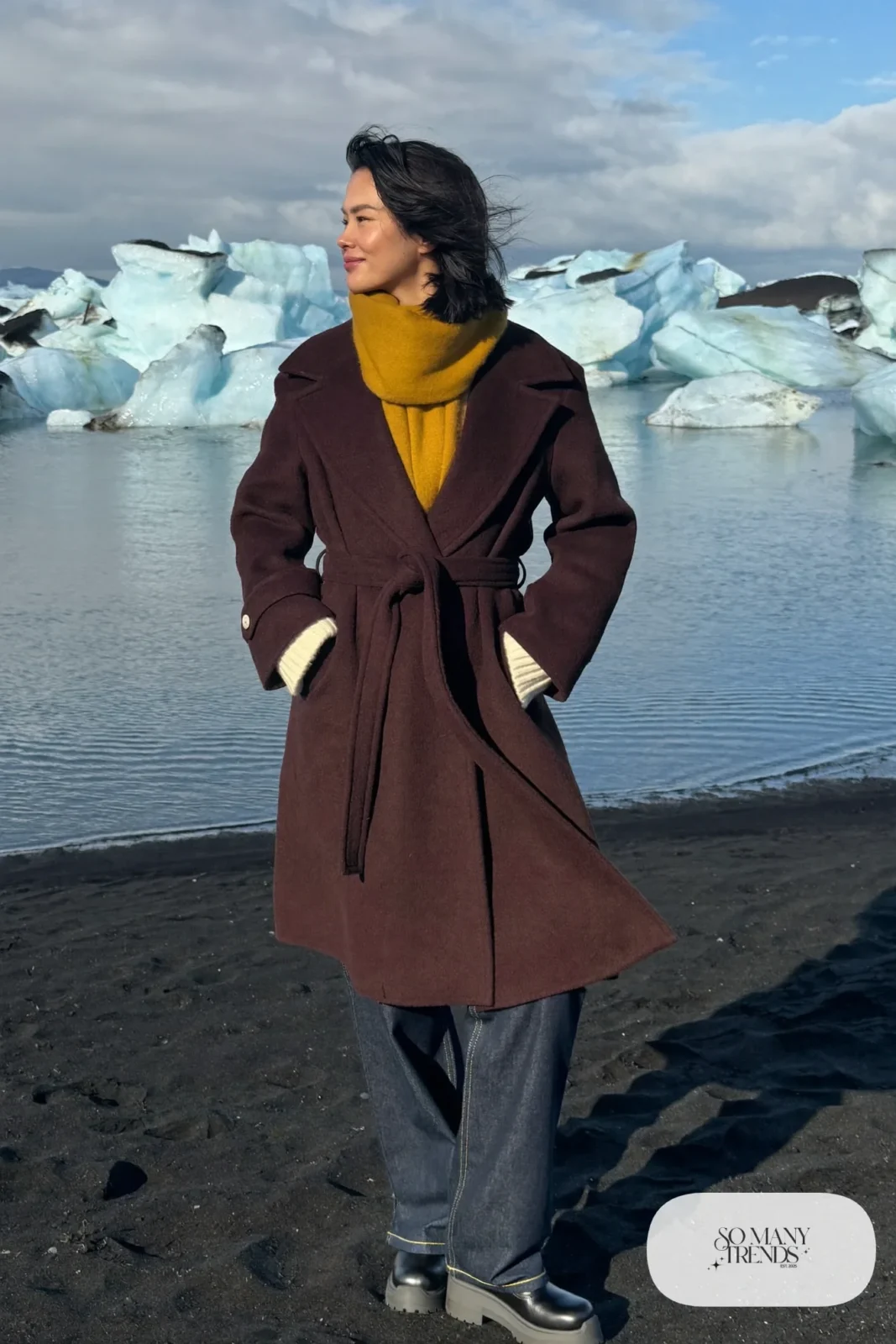 Woman in a burgundy belted wool coat, cream sweater, wide dark jeans and lug-sole boots at glacier lagoon, outfit 12