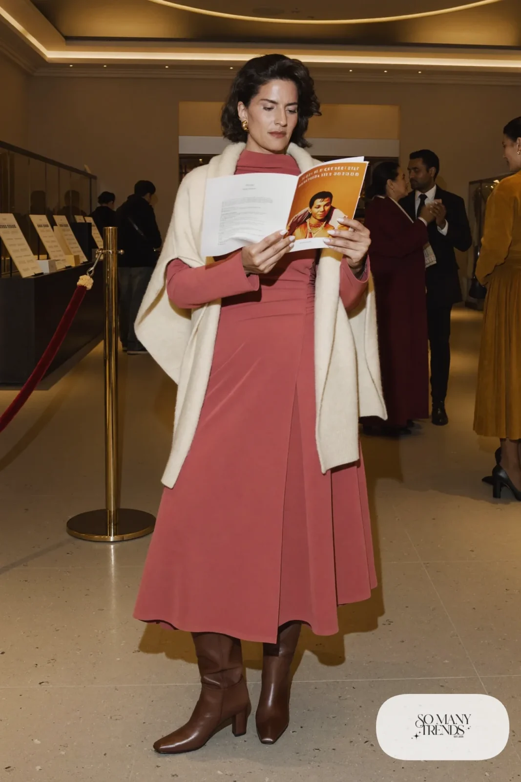 Woman in a dusty pink wrap midi dress, cream cashmere wrap draped over shoulders and brown knee-high boots, theater outfit 2