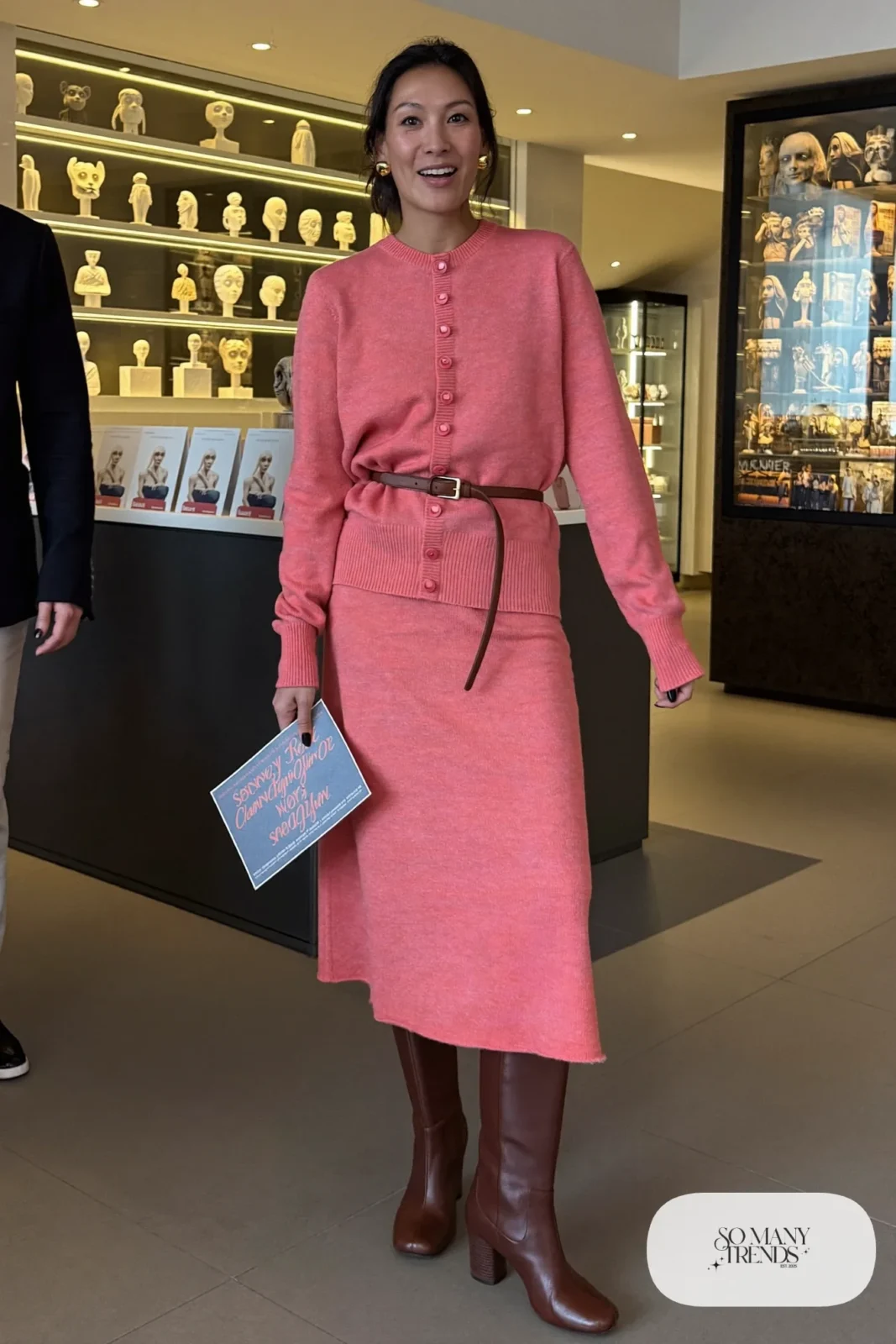 Woman in a dusty pink fine knit cardigan and matching midi skirt set with thin belt and brown knee-high boots, theater outfit 11