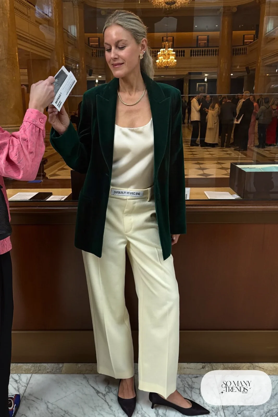 Woman in a forest green velvet blazer, cream wide-leg pants, ivory shell top and black pointed flats, theater outfit 16