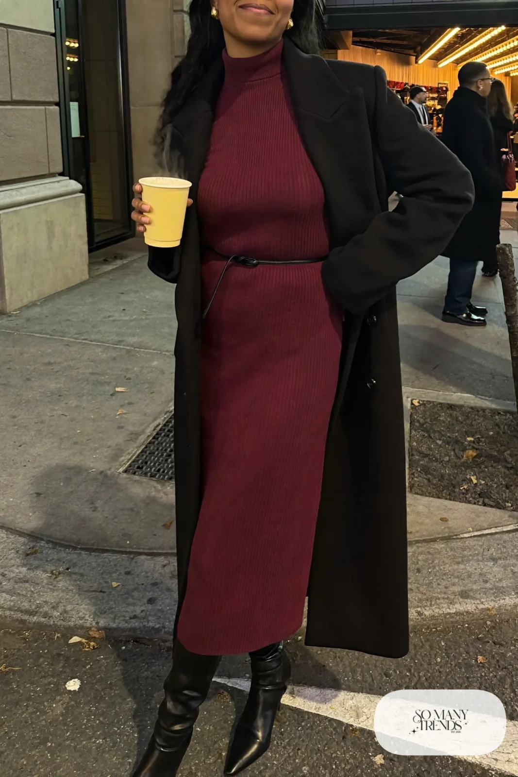 Woman in a burgundy ribbed knit midi dress with belt, long black coat and black knee-high boots, theater outfit 22