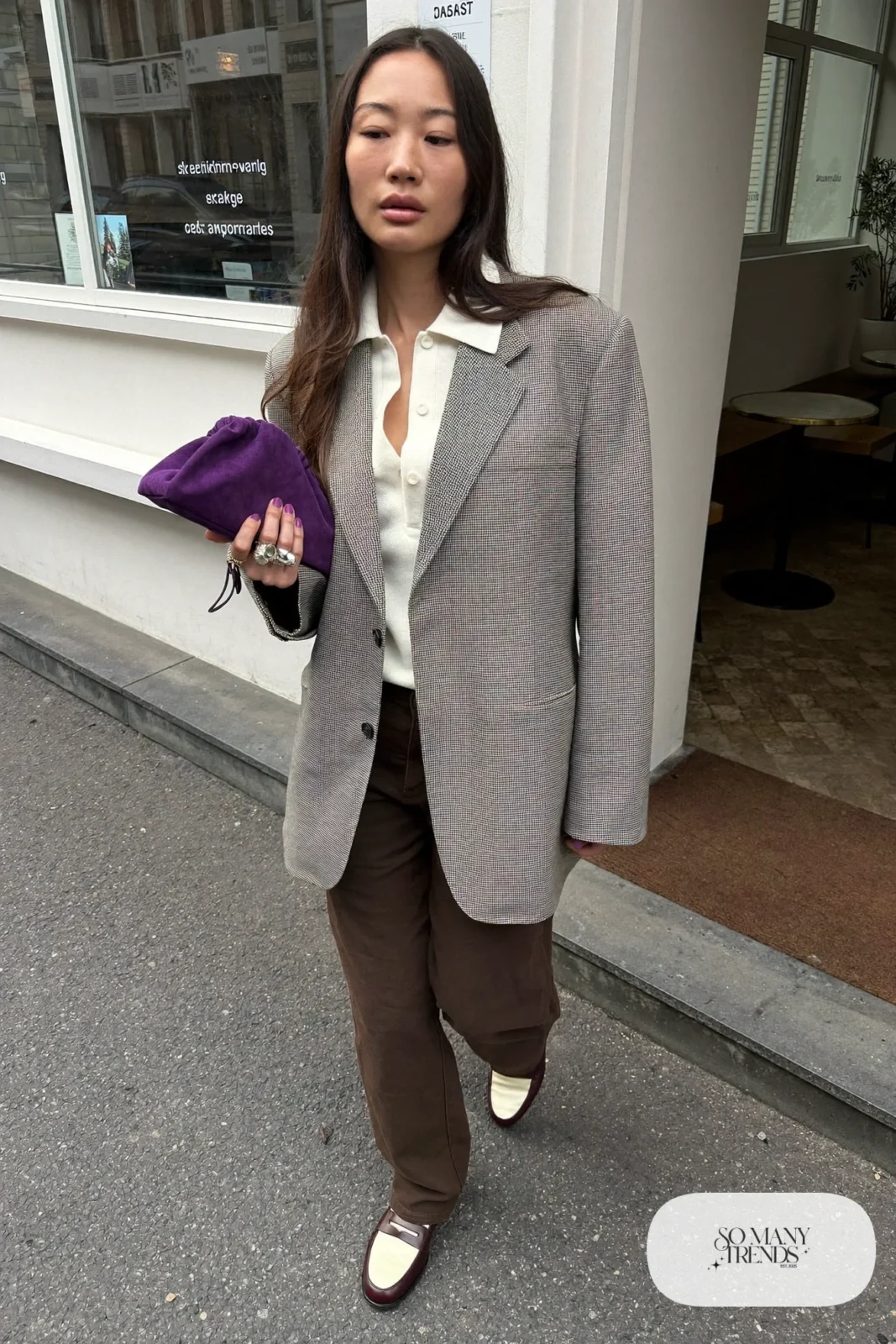 Woman in an oversized gray check blazer, pearl knit polo sweater, chocolate straight pants and two-tone loafers holding a small purple pouch bag, outfit 8