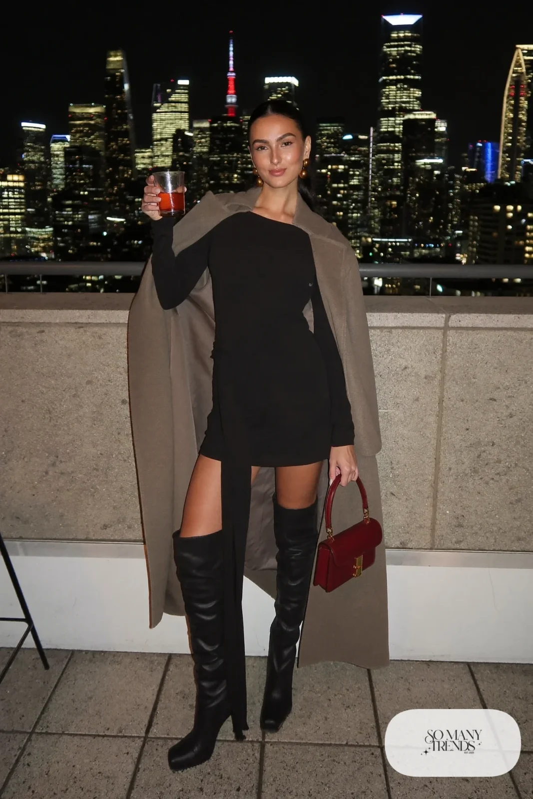 Woman in a taupe wool cape coat with attached scarf over a black boat-neck mini dress and black over-the-knee boots with a burgundy bag, outfit 14