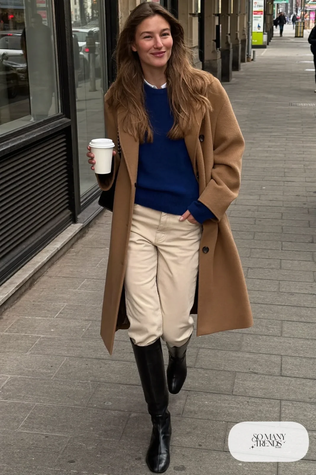 Woman in long camel coat, ink blue sweater, cream straight pants and black tall leather riding boots, outfit 1