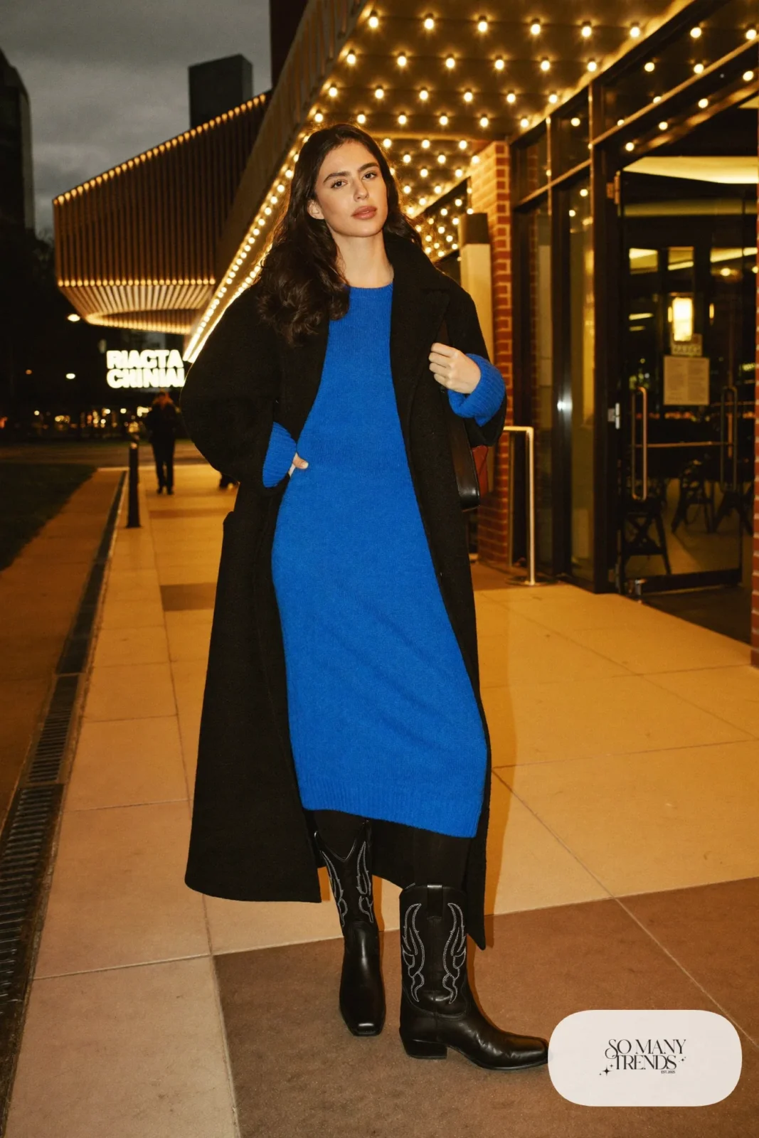Woman in cobalt sweater dress, black tights, black western boots and long black coat, outfit 24