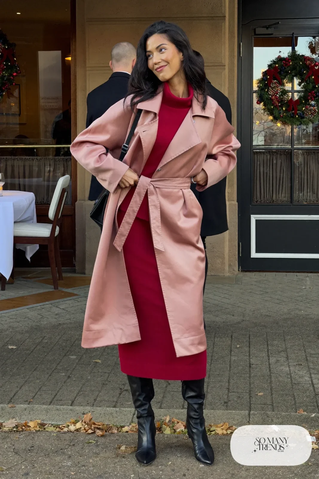 Woman in blush belted wrap coat, wine knit midi dress with high neck and black tall boots, outfit 24