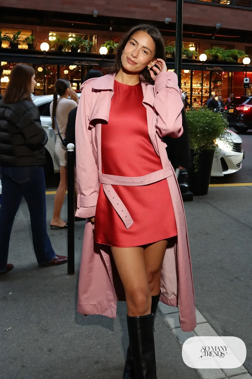 Woman in a blush pink trench coat over a tomato red mini dress with black knee-high boots, outfit 5