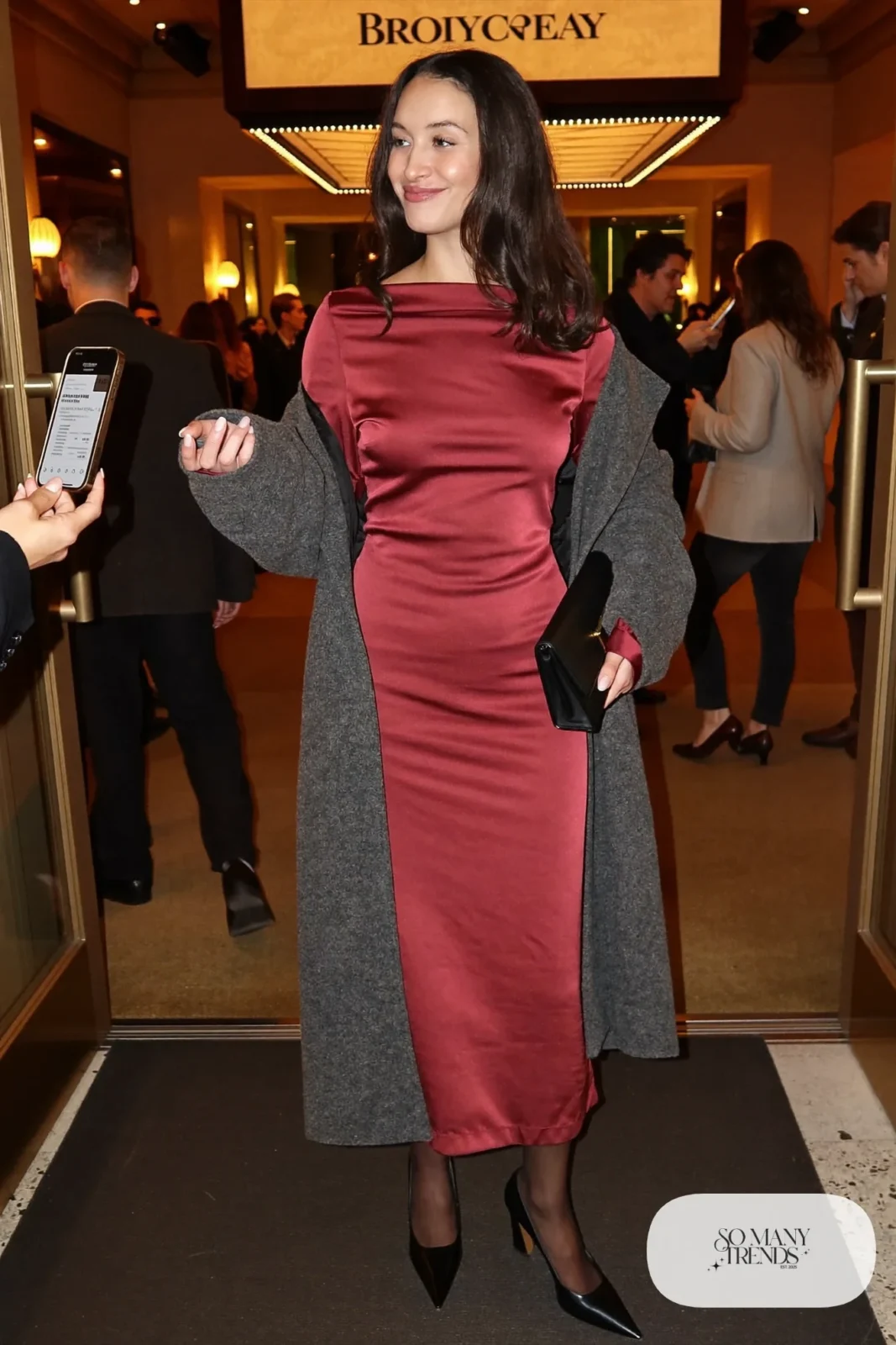 Woman in a burgundy satin midi dress, relaxed gray wool coat, sheer black tights and black block-heel pumps, theater outfit 1