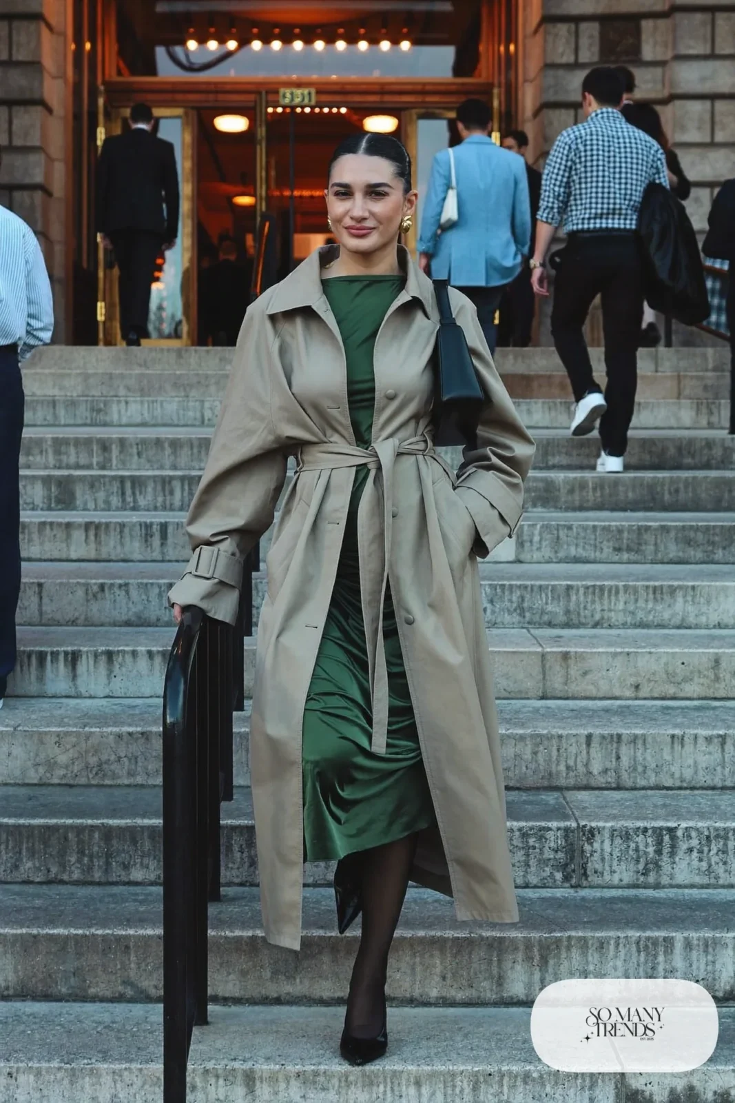 Woman in a forest green midi dress, beige belted trench coat, sheer tights and black pumps, theater outfit 5
