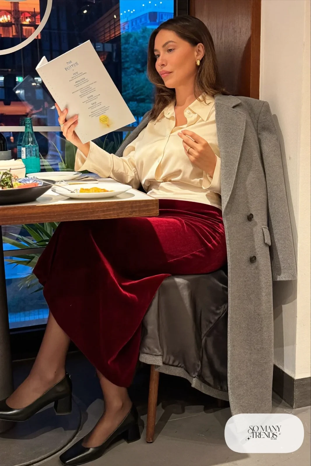 Woman in a burgundy velvet midi skirt, cream satin blouse buttoned to the collarbone, gray wool coat and black block-heel pumps, theater outfit 9