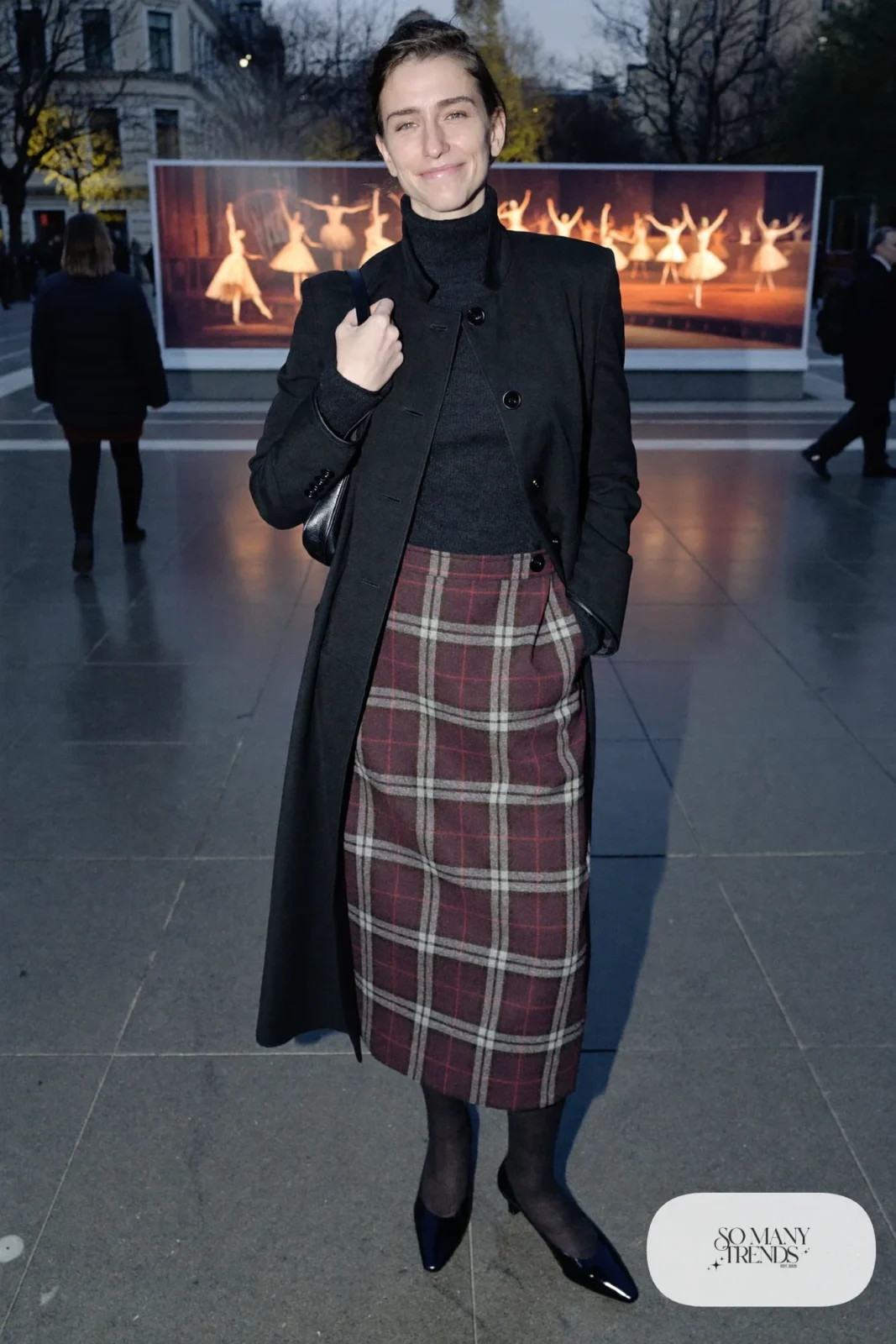 Woman in a gray and burgundy plaid wool midi skirt, black merino turtleneck, black wool coat and black low-heel pumps, theater outfit 10