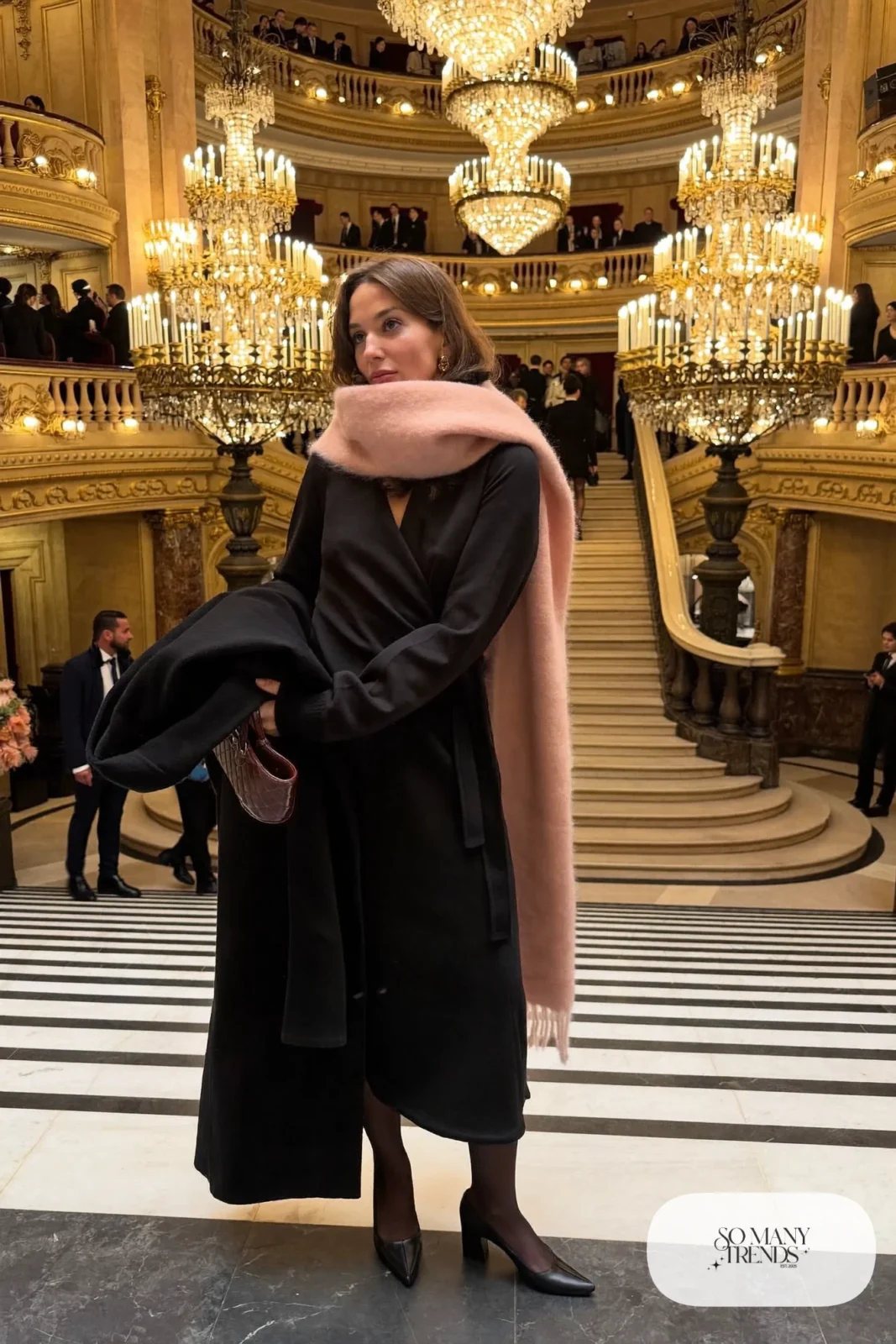 Woman in a black wrap midi dress, dusty pink cashmere scarf, long black coat and black block-heel pumps, theater outfit 25