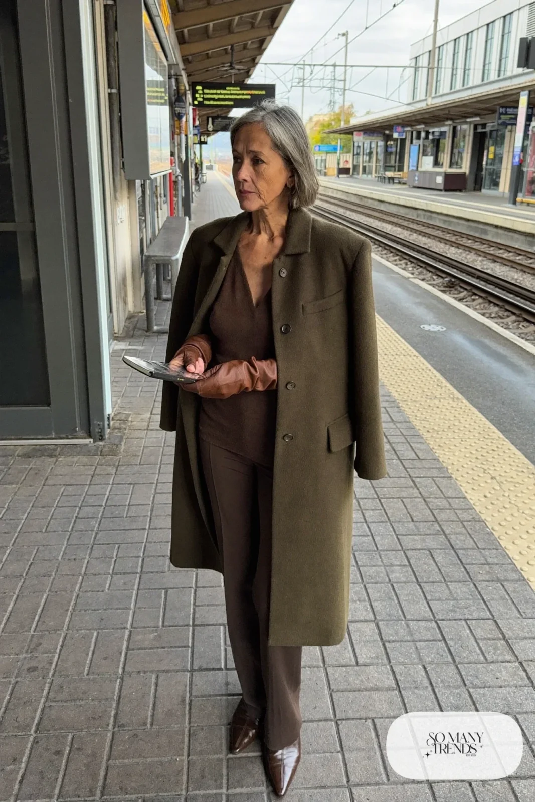 Petite woman in a knee-length olive coat over a chocolate brown knit top and pants with brown boots and gloves, outfit 14