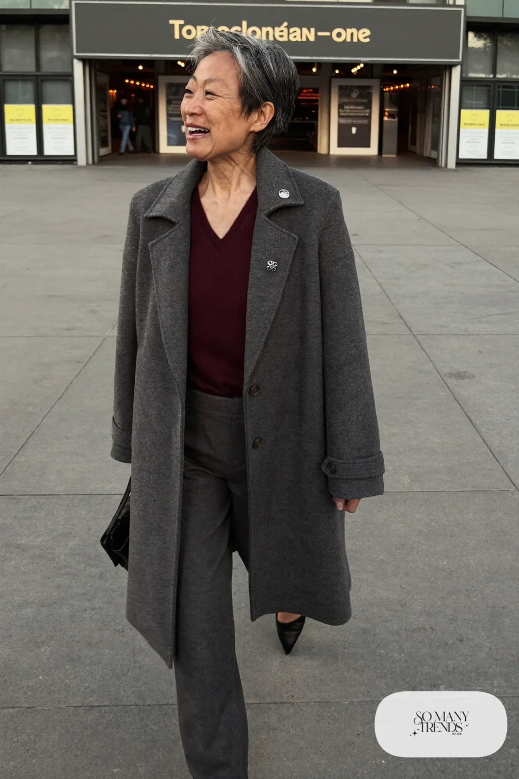 Petite woman in a knee-length charcoal coat over a burgundy knit and charcoal pants with black flats, outfit 18