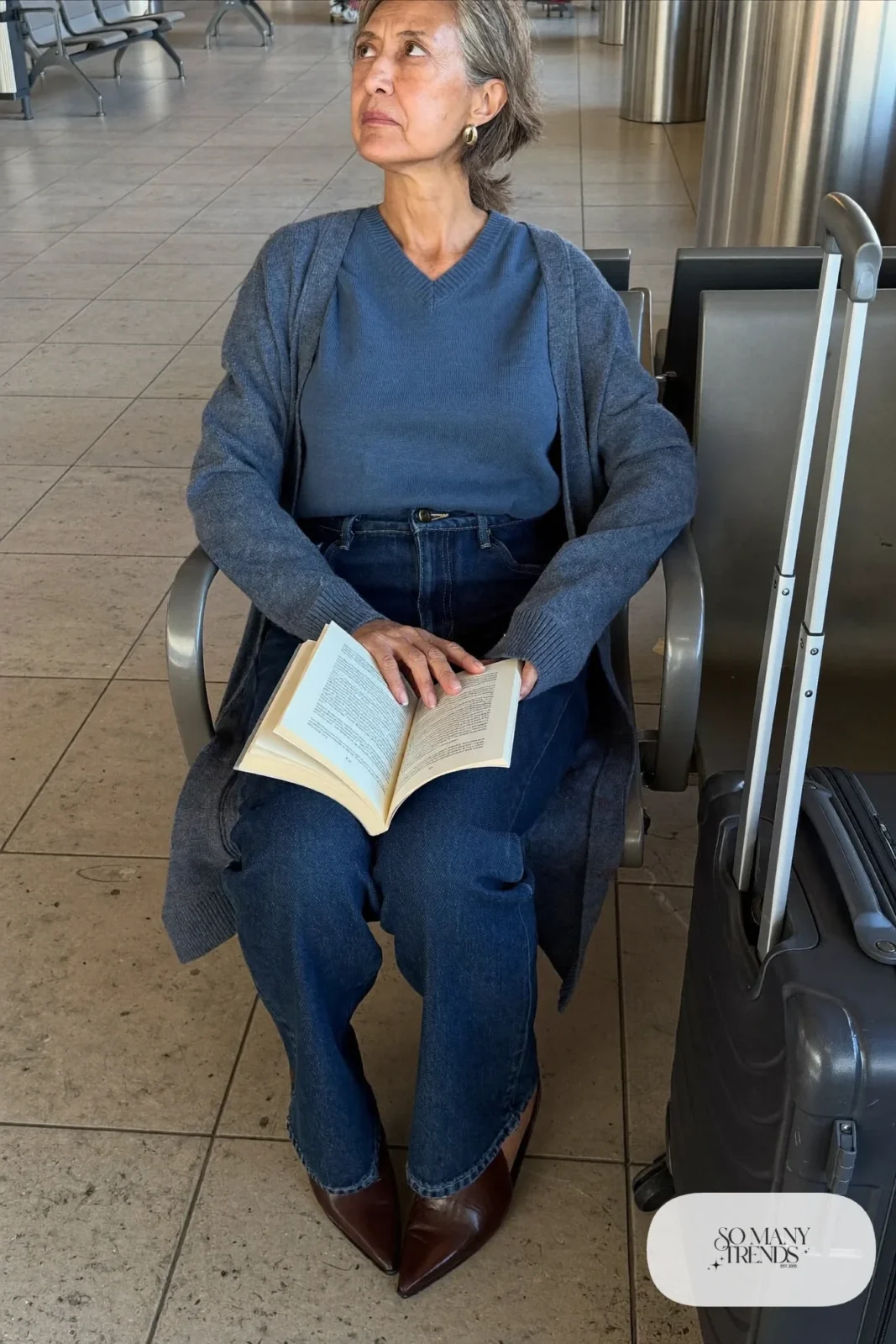 Petite woman in dark straight jeans, slate-blue knit and hip-length blue cardigan with brown loafers while traveling, outfit 20