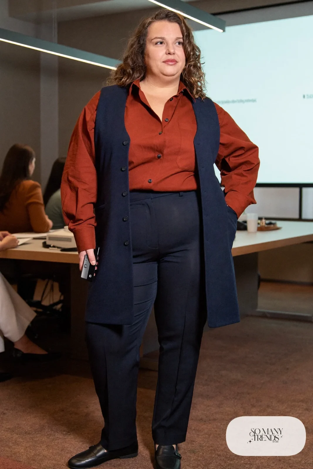 Woman in rust cotton shirt, ink navy tailored longline vest, navy straight pants and black loafers, outfit 3