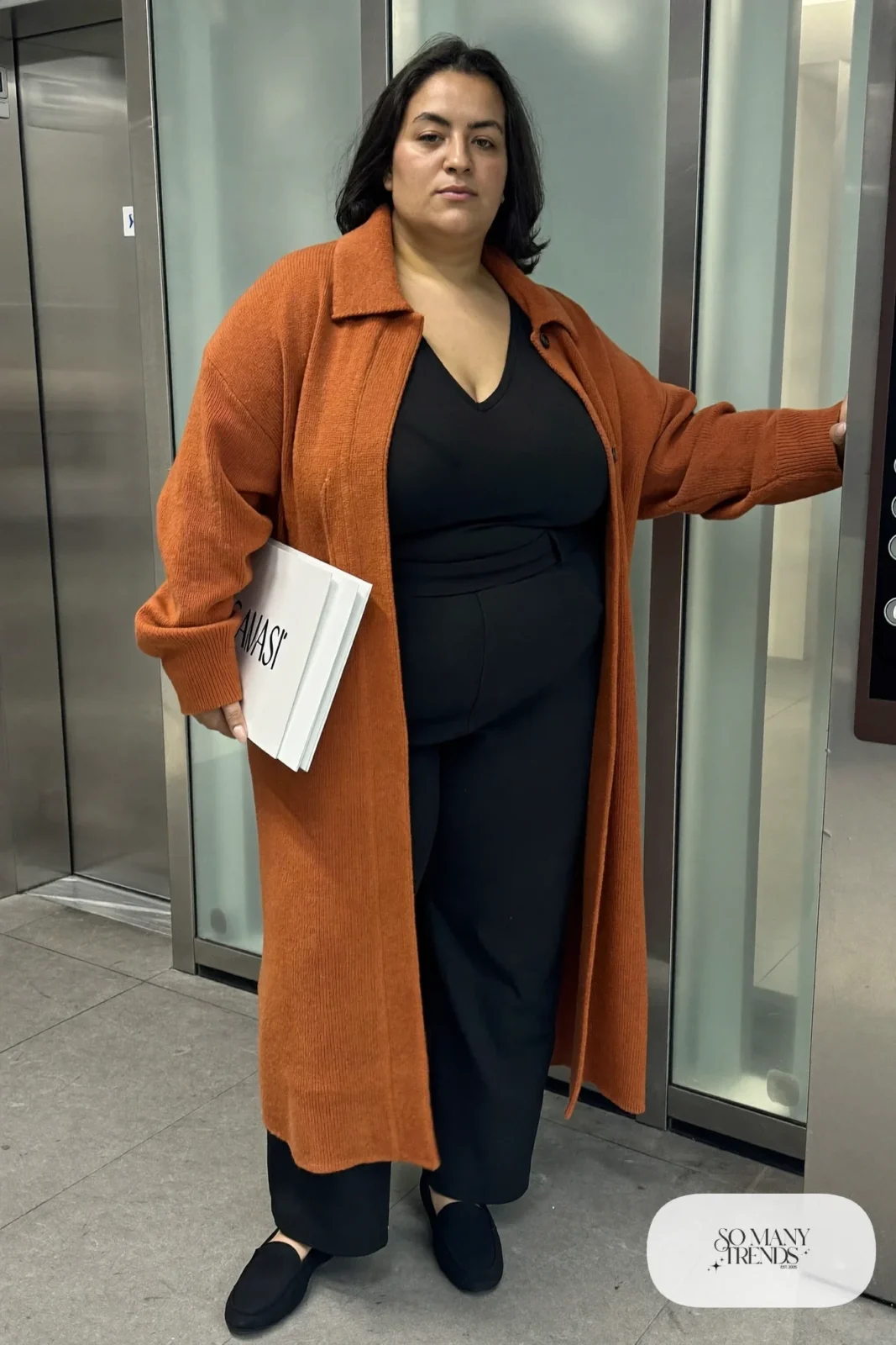 Woman in rust longline knit cardigan coat, black V-neck tee, black straight pants and black loafers, outfit 13