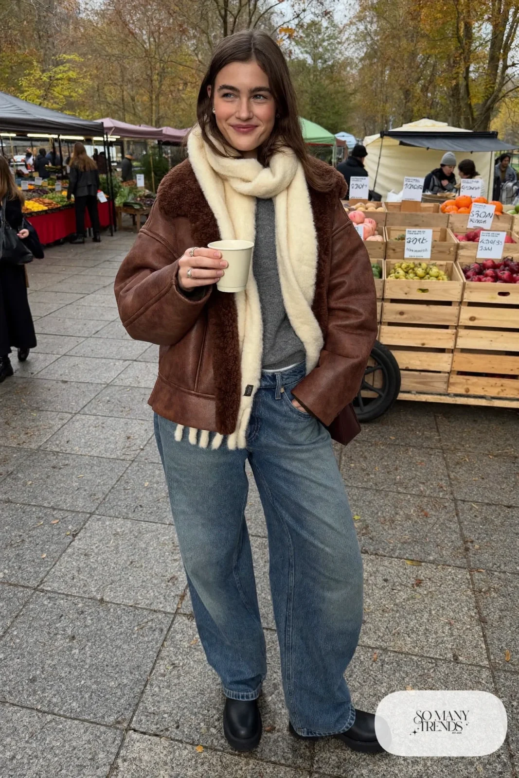 Woman in curved indigo jeans, cognac faux shearling jacket, cream scarf and lug-sole boots, look 4