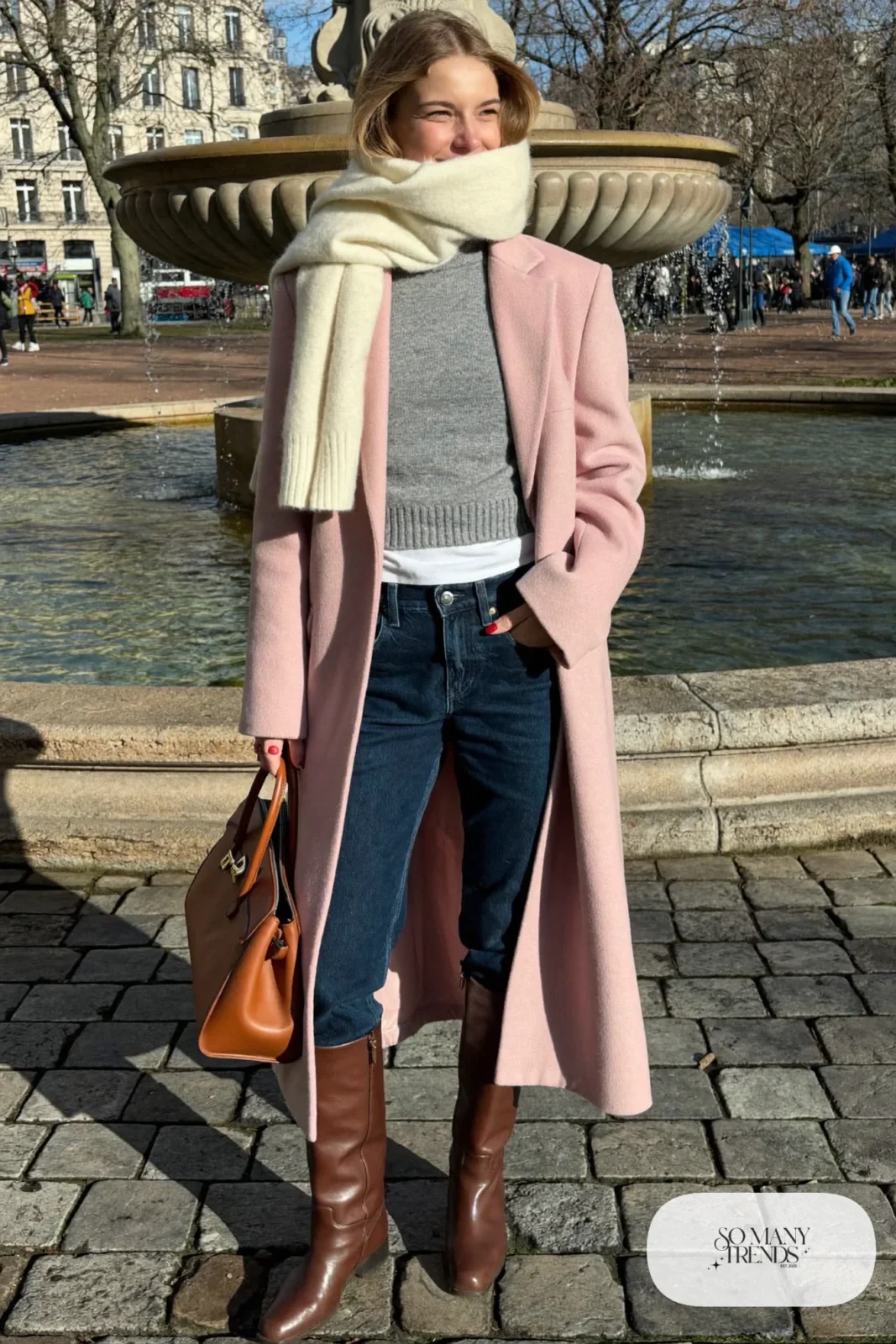 Woman in straight jeans tucked into tall brown boots, long dusty pink coat and cream scarf, look 17
