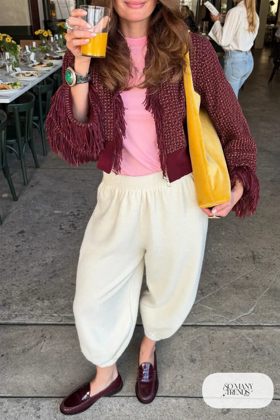 Woman in cream knit balloon pants, baby-pink tee, burgundy fringe boucle jacket and burgundy loafers, look 25