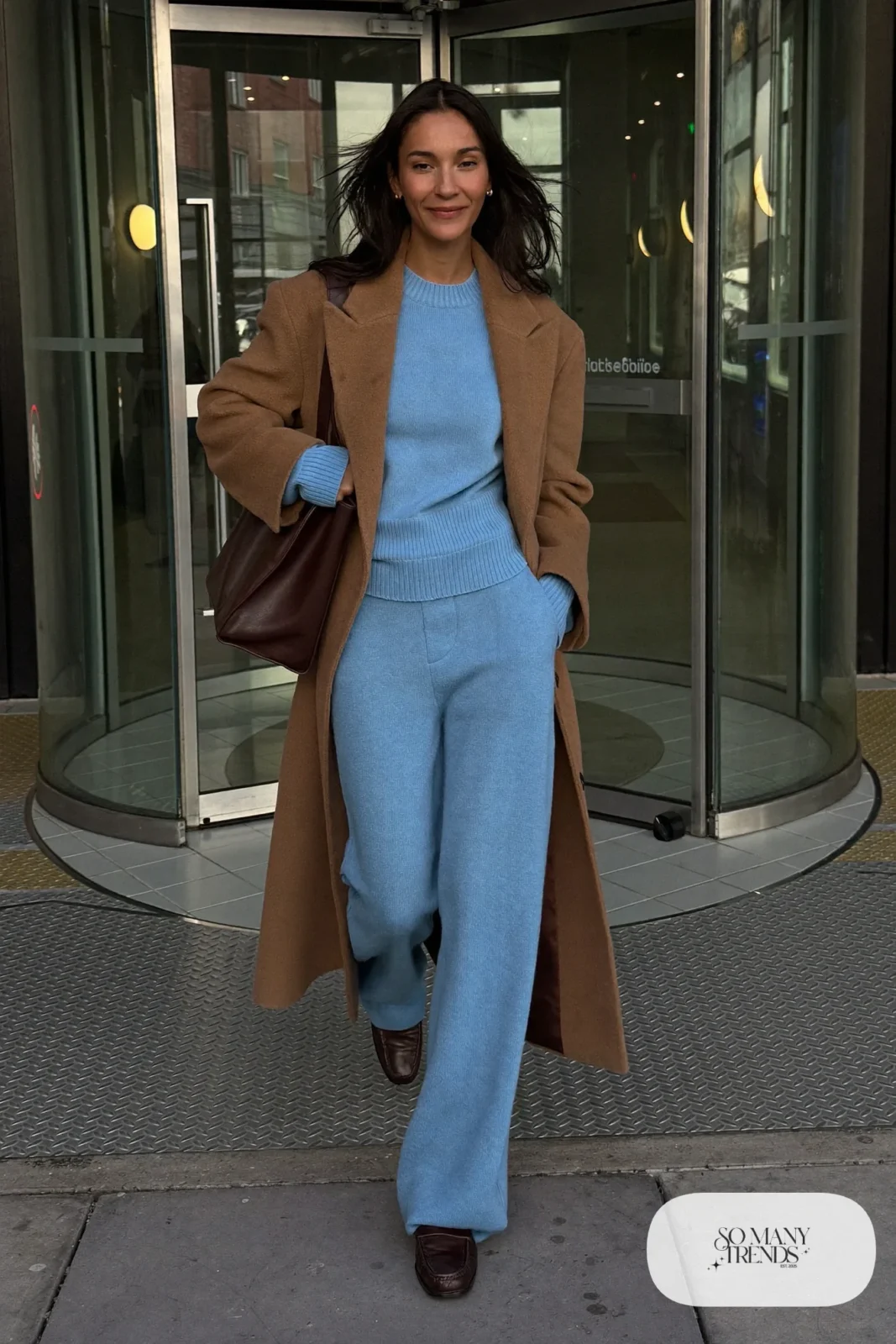 Woman in a sky blue knit sweater and matching pants with a long camel coat and brown loafers, outfit 12