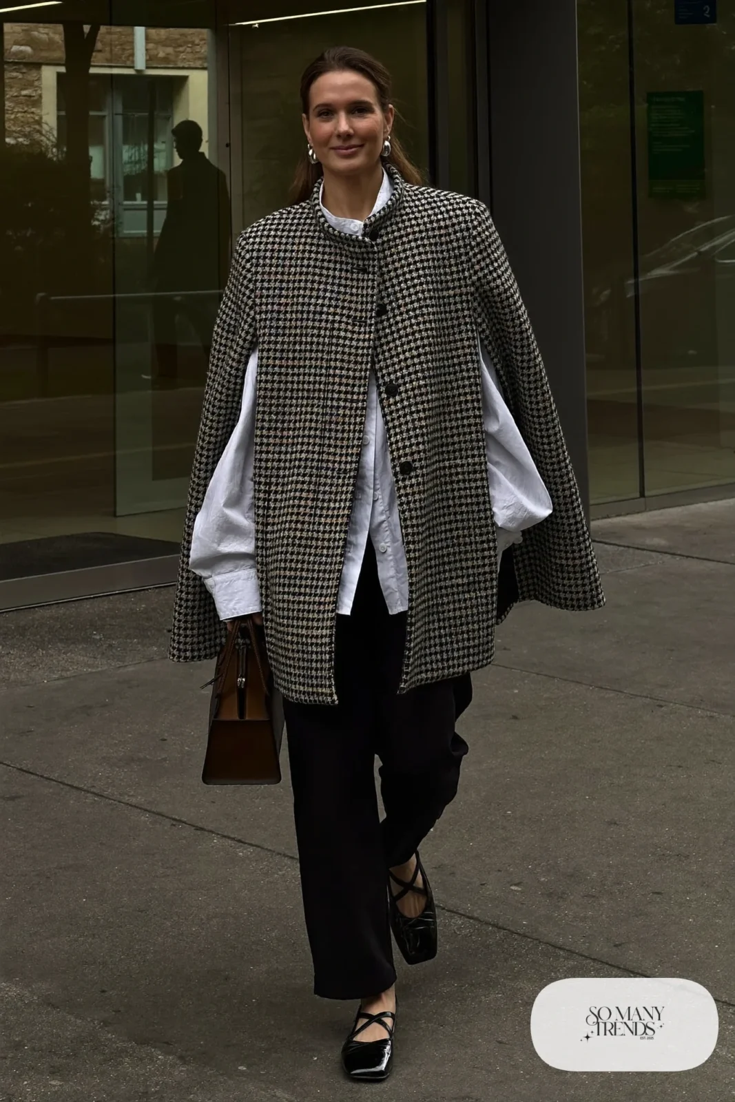 Woman in a houndstooth tweed cape over a white shirt, black pants, flats and a structured bag, outfit 20