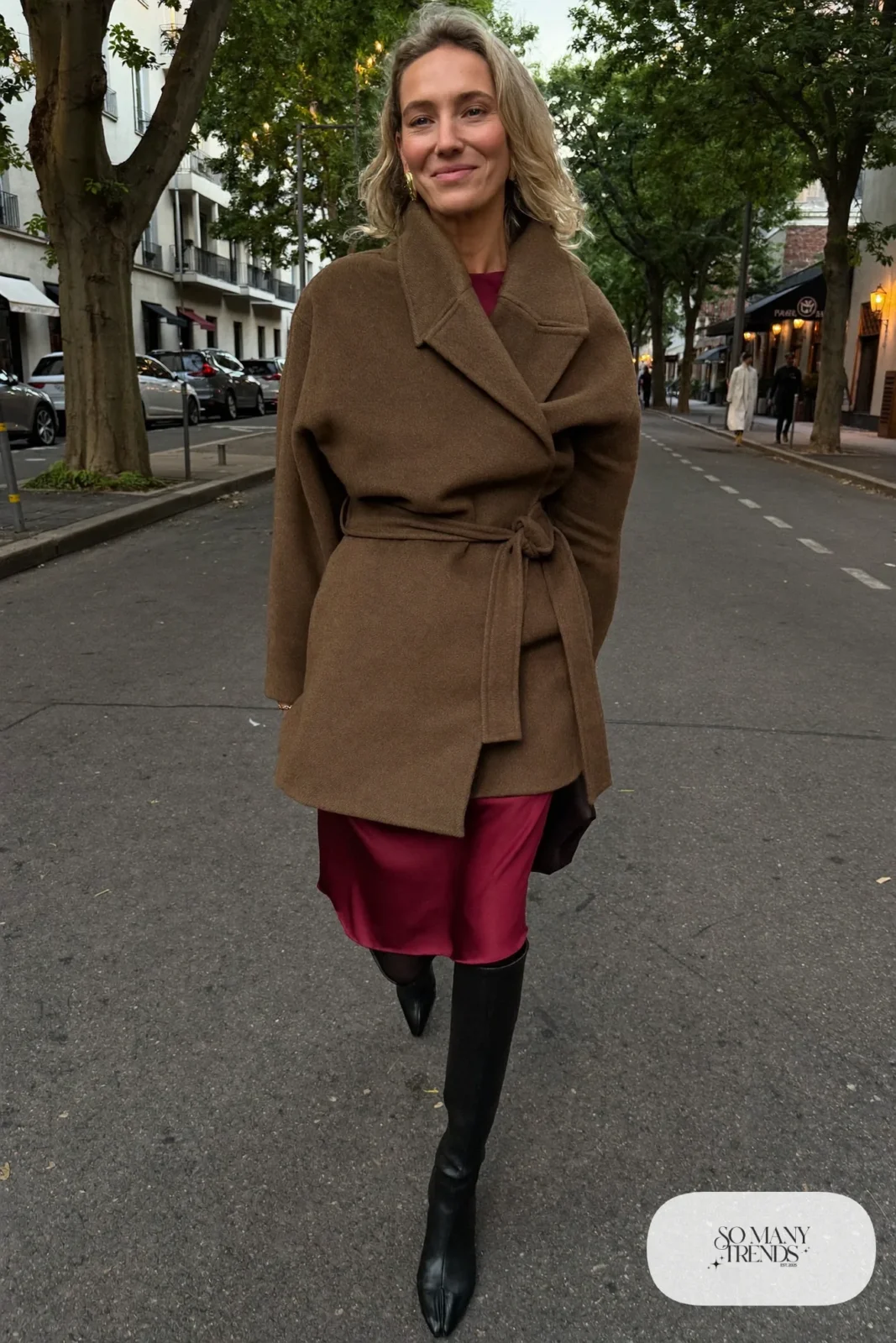 Woman in a belted chocolate brown wool coat over a wine satin midi dress with tall black boots, outfit 20