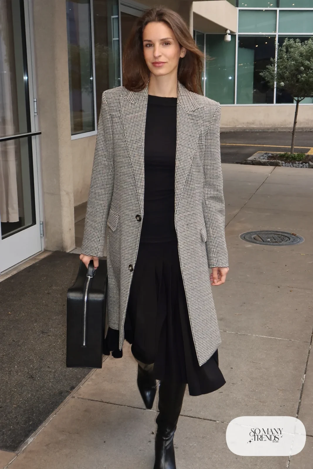 Woman in a houndstooth wool coat-blazer, black pleated midi skirt, fitted black knit, sheer black tights and black knee boots, outfit 25