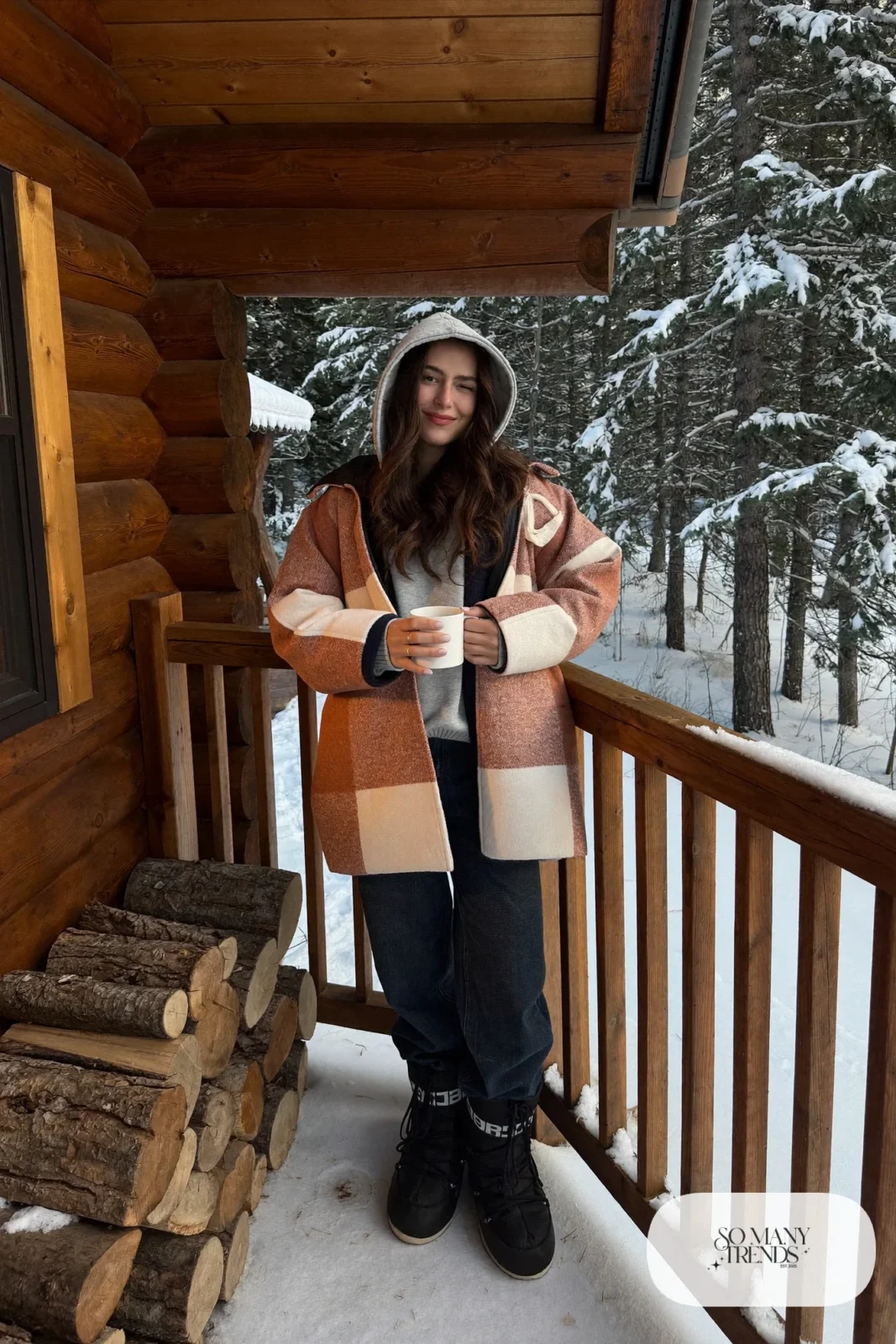 Woman in terracotta and cream plaid shacket, gray hoodie, dark jeans and black moon boots on a cabin porch, outfit 10