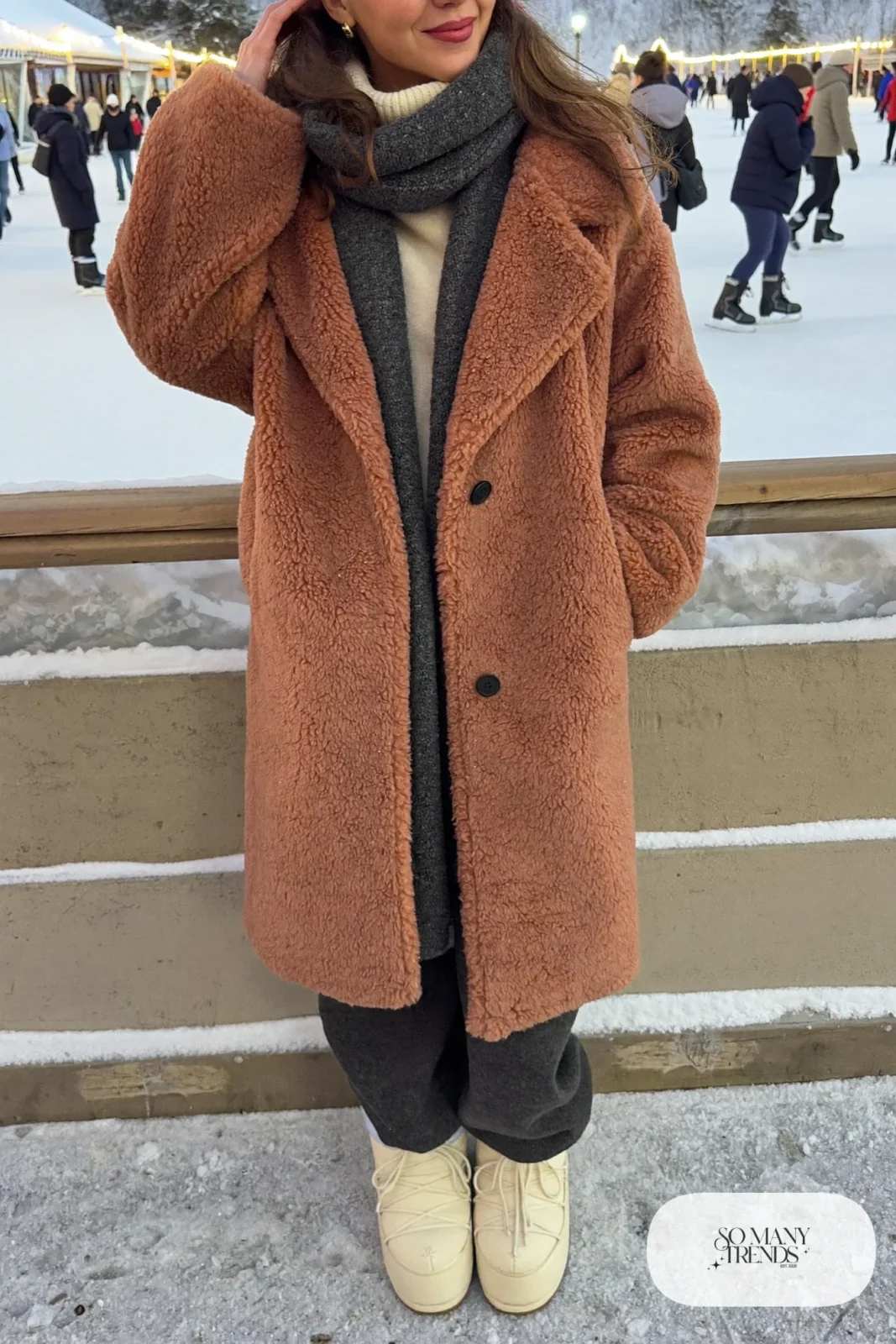 Woman in terracotta teddy fleece coat, cream turtleneck, charcoal pants and cream moon boots in the snow, outfit 22