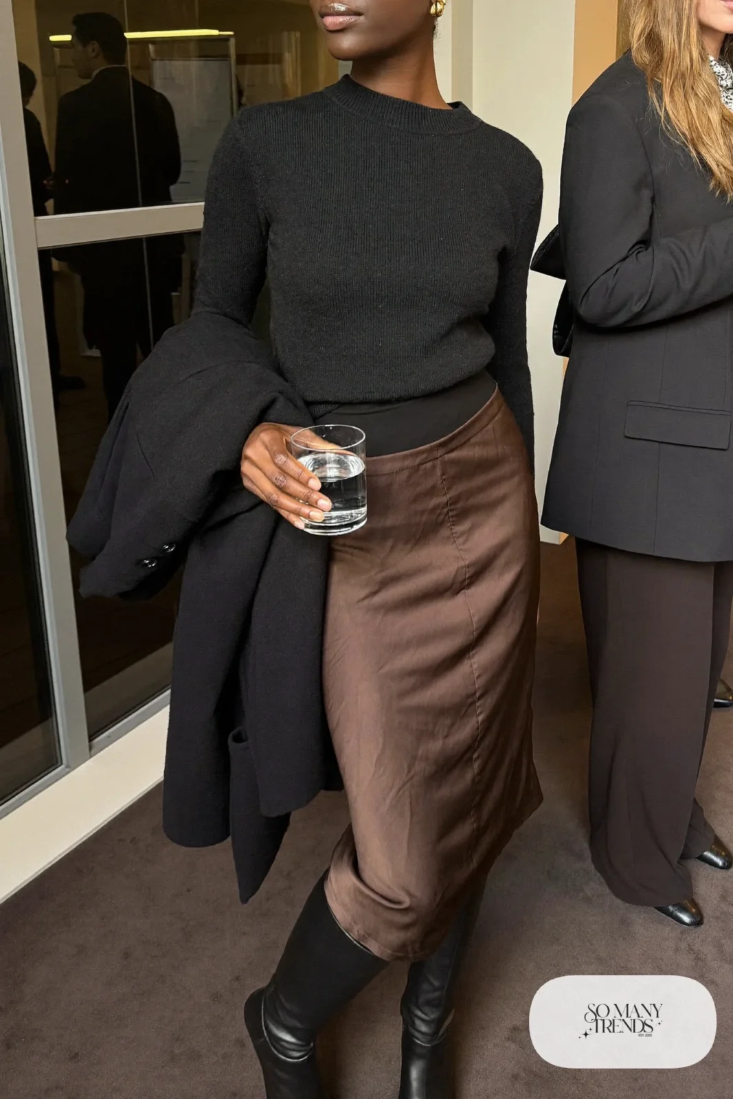 Woman in chocolate brown satin midi skirt, black fine knit sweater, black opaque tights and tall black boots, outfit 3