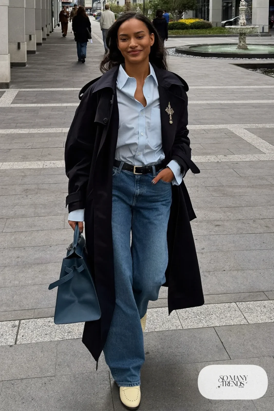 Woman in pale blue poplin shirt, mid-blue wide-leg jeans, navy belted coat and cream loafers, outfit 19