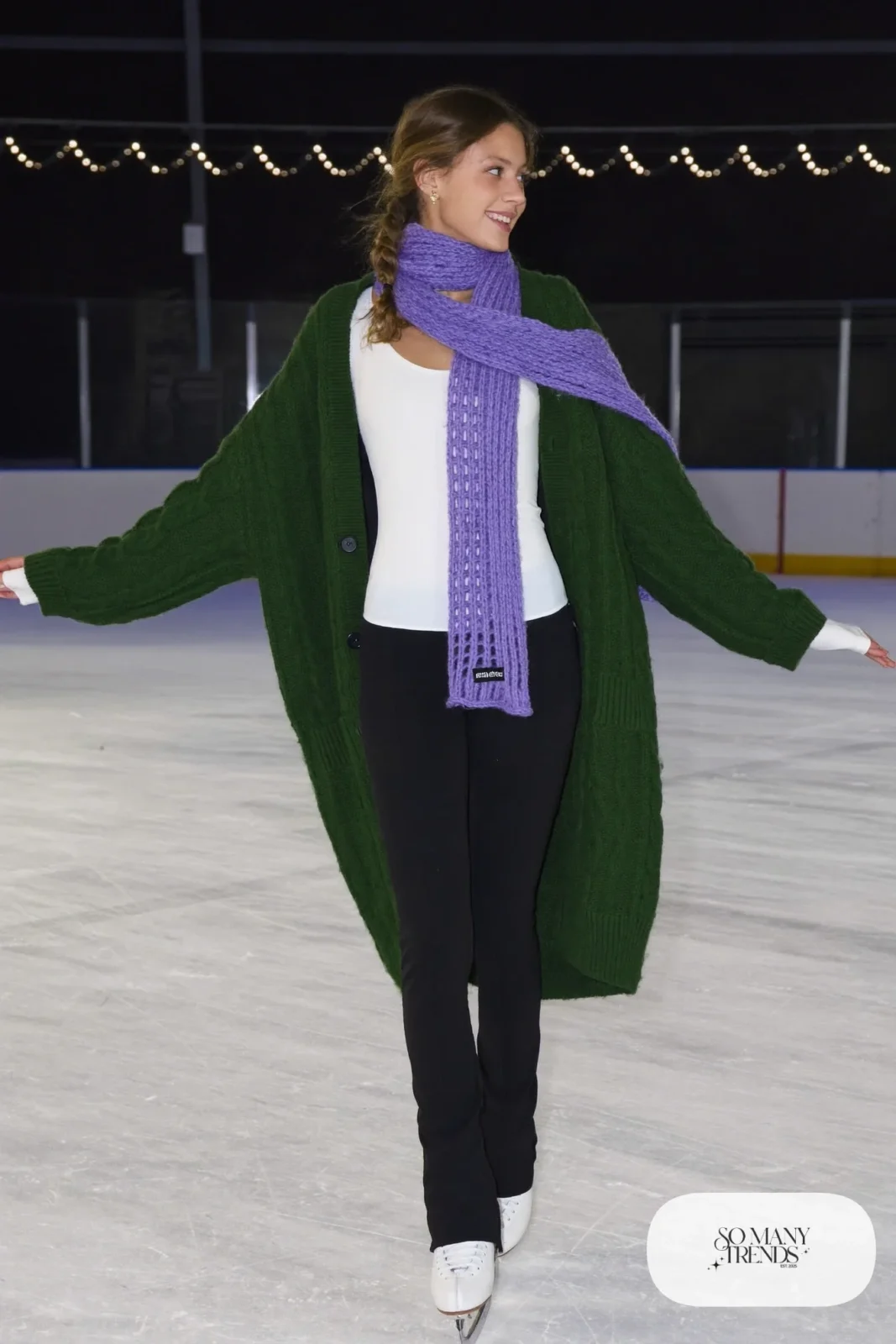 Forest green chunky cable-knit cardigan over white thermal top, black stretch pants, lilac scarf and ice skates - outfit 26