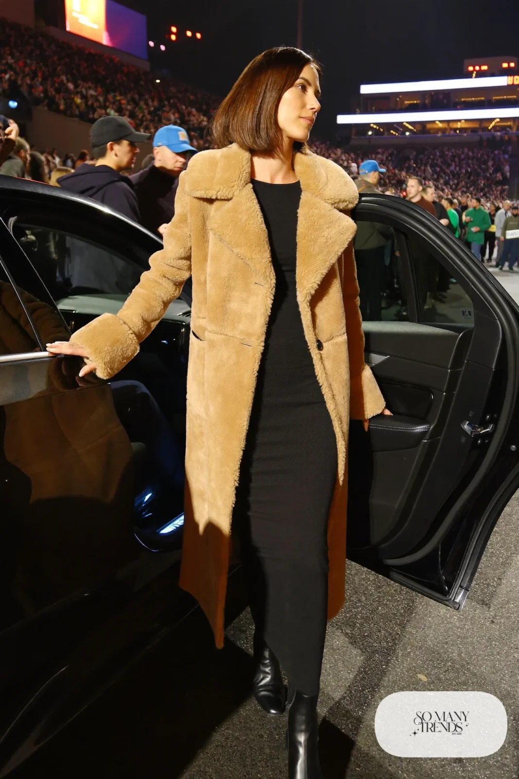 Woman in long camel shearling coat, black knit top and pants and black boots, NFR outfit 25