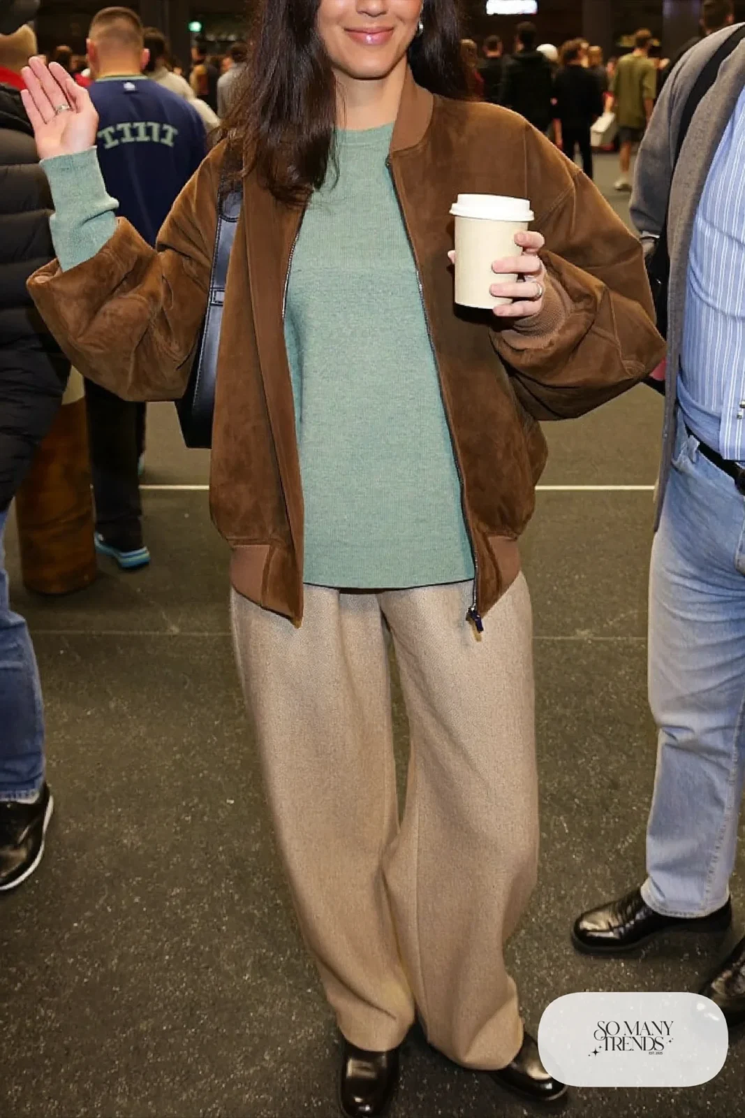 Woman in an espresso suede bomber, sage knit sweater, wide-leg oatmeal wool pants and black loafers, basketball game outfit 1