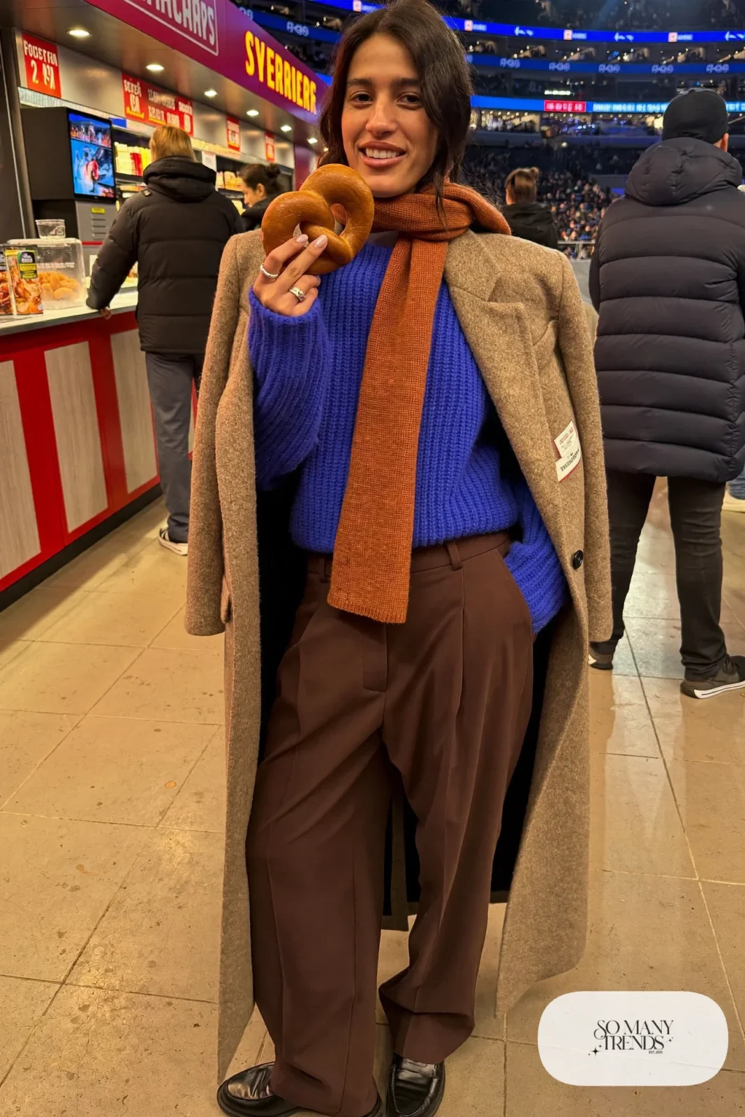 Woman in a cobalt blue sweater, rust knit scarf, chocolate wide pants and black loafers, basketball game outfit 5