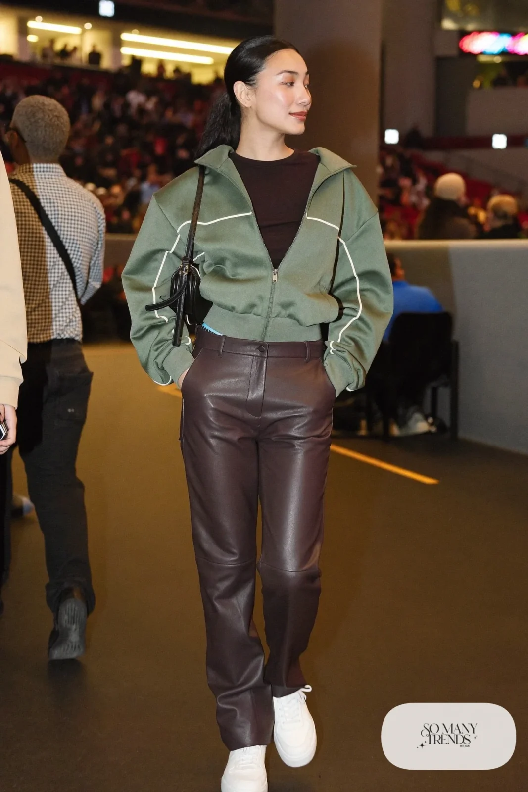 Woman in a sage track jacket, black tee, espresso faux leather pants and white sneakers, basketball game outfit 7