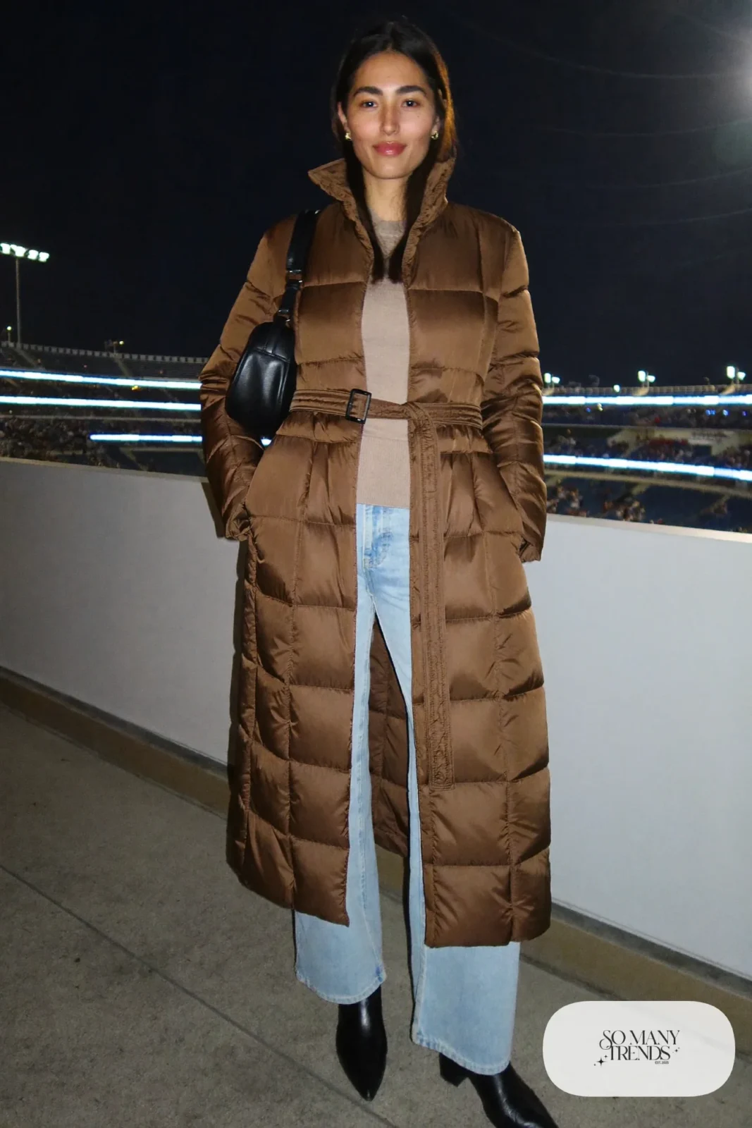 Woman in a long belted espresso quilted coat, thin knit, wide jeans and black boots, basketball game outfit 20