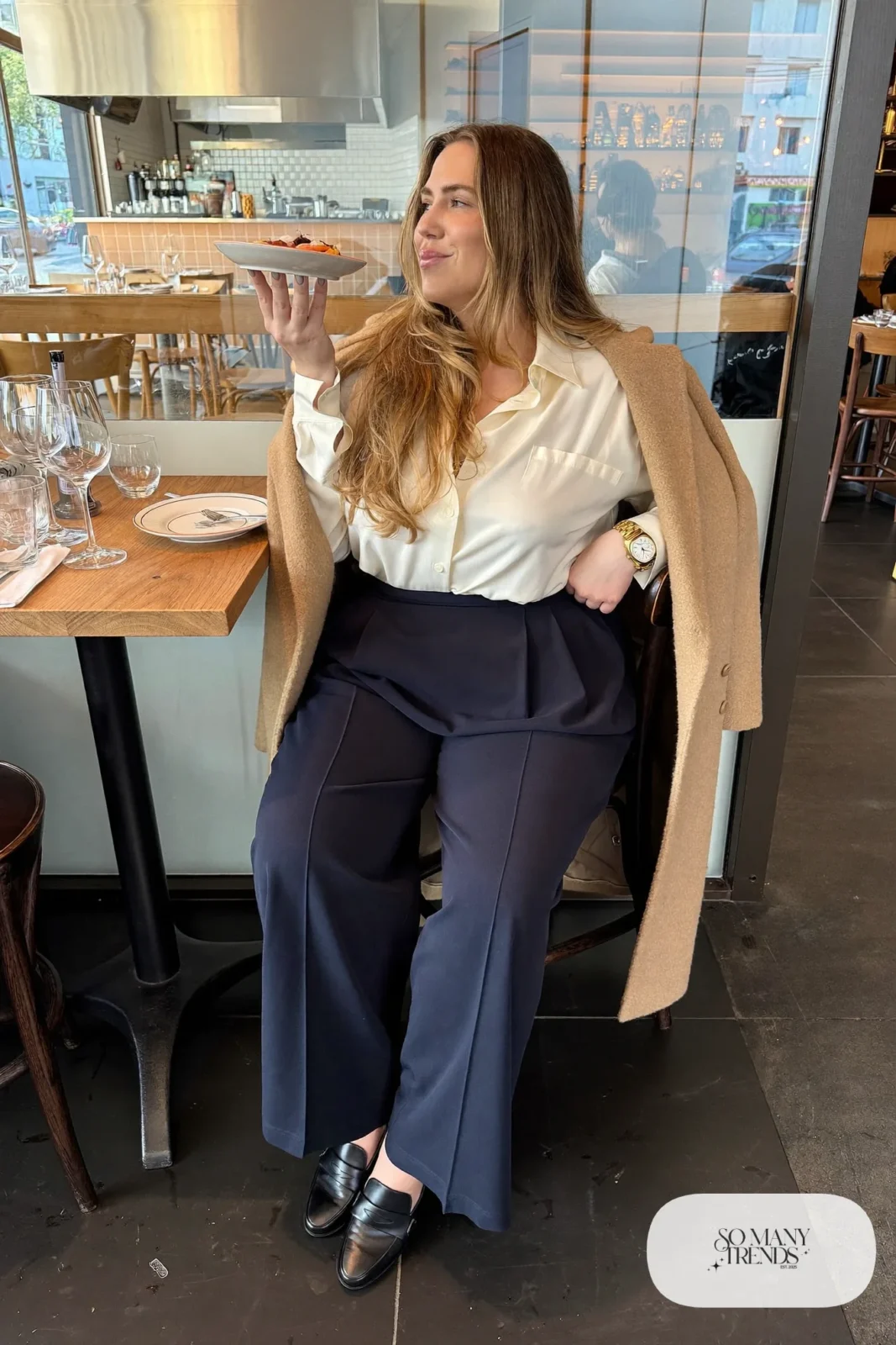 Plus size woman in navy wide-leg pants, ivory silk-feel shirt, camel coat and black loafers, outfit 16