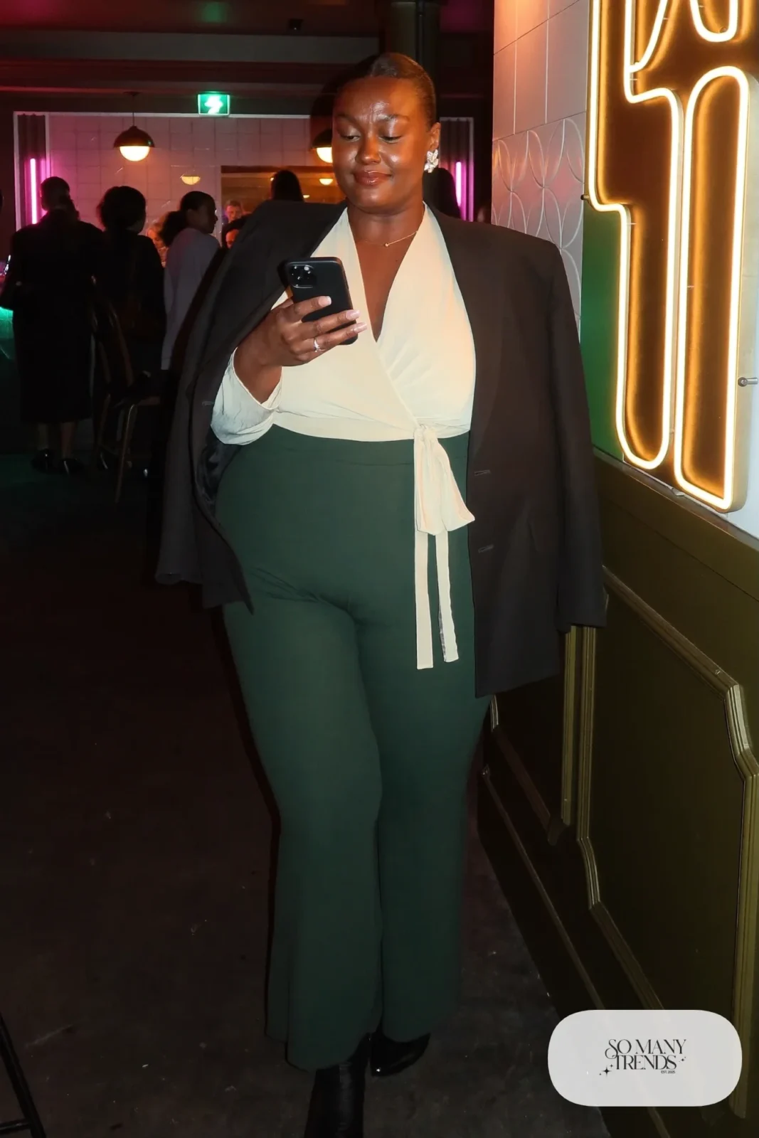 Plus size woman in dark green flare pants, ivory wrap top, black blazer and black heeled boots, outfit 18