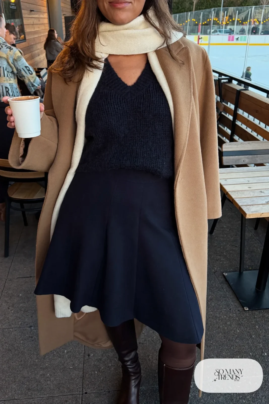 Plus size woman in navy knit skirt set with ivory scarf, camel coat and brown boots, outfit 24