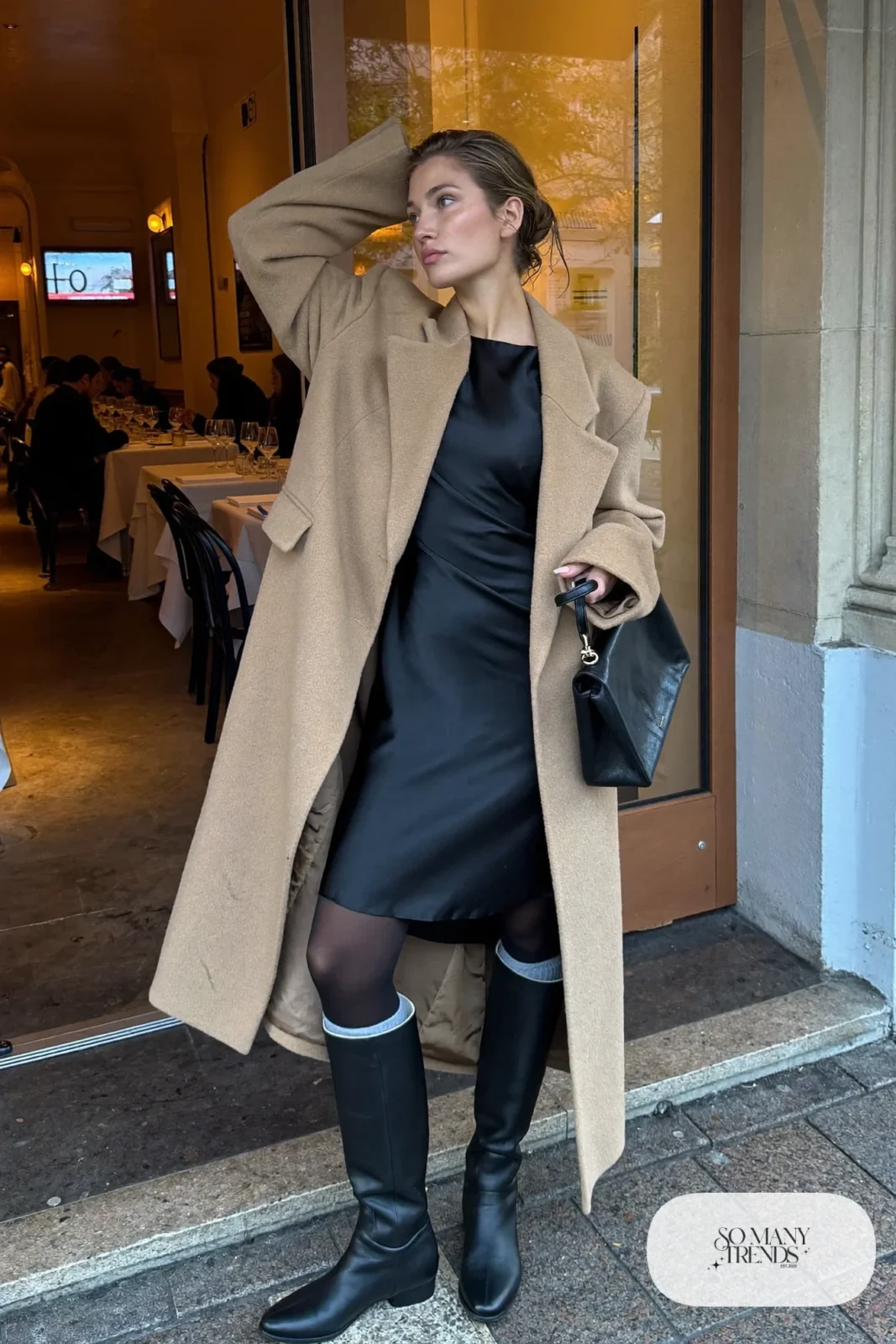 Long camel wool coat over black satin midi slip dress with black knee-high boots and small black bag, winter date outfit 2