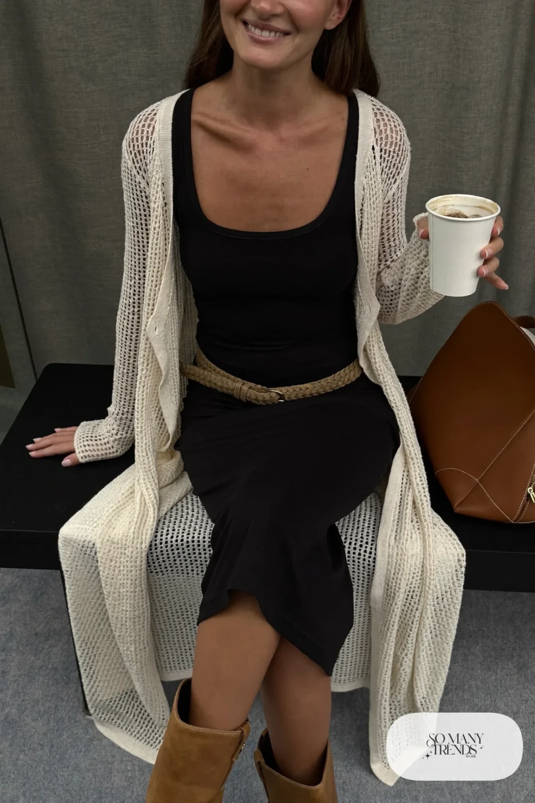 Woman in cream knit cardigan over black tank dress with woven belt and tan boots, outfit 21