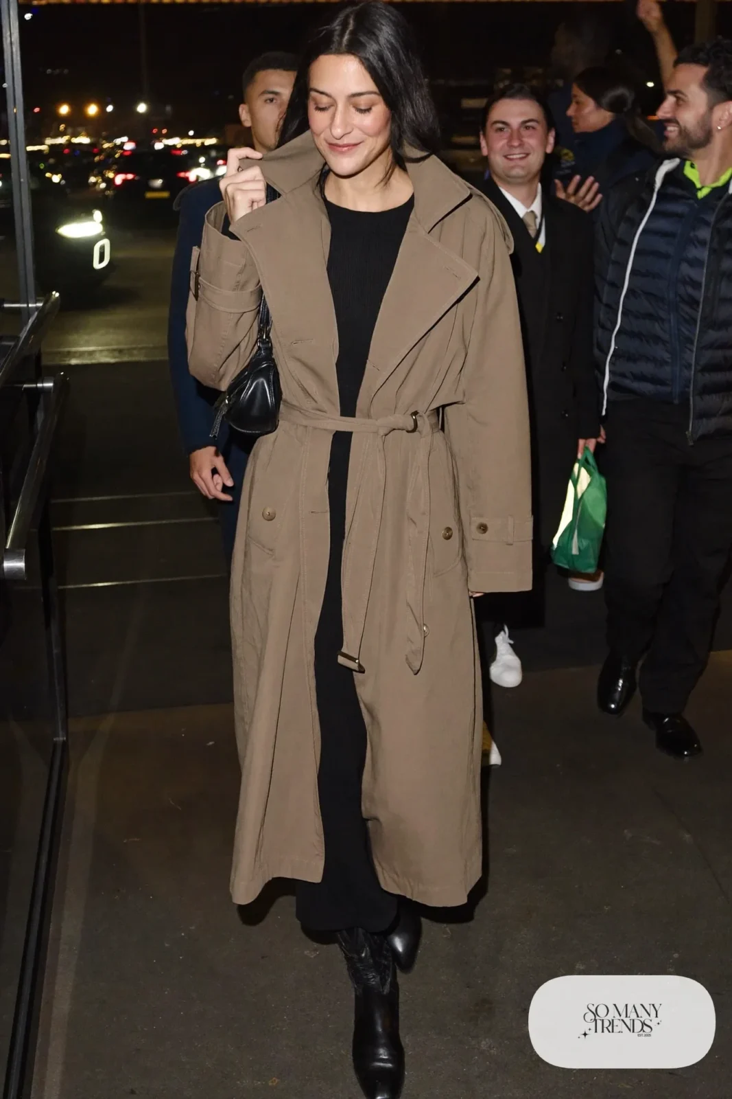 Woman in lightweight taupe trench coat over black dress with black boots, outfit 26