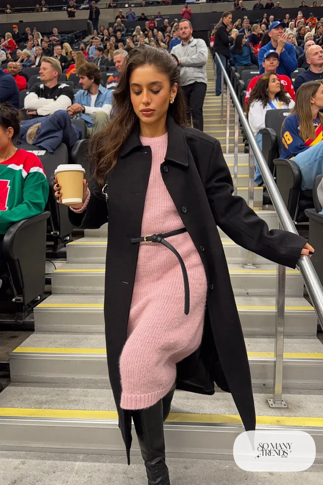 Woman in pale pink chunky knit midi sweater dress, black belt, black opaque tights and black knee-high boots, hockey game outfit 4
