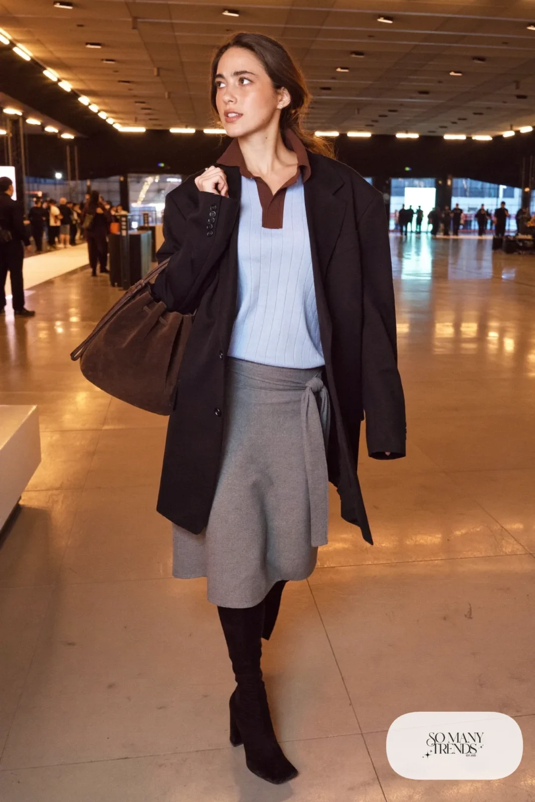 Woman in pale blue ribbed knit polo, gray knotted skirt, black oversized blazer, black tights and over-the-knee boots, hockey game outfit 20