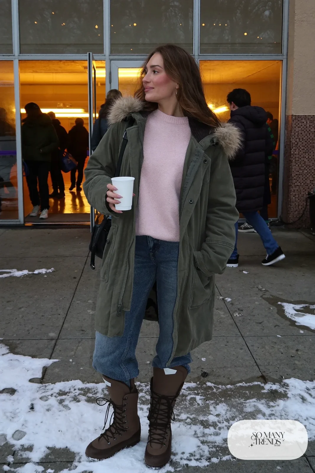 Woman in long olive parka with fur-trim hood, pale pink knit sweater, straight jeans and brown waterproof boots, hockey game outfit 21