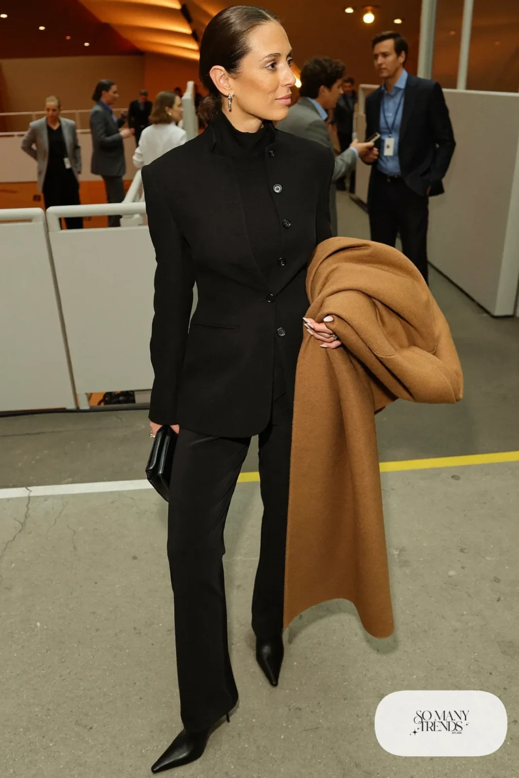 Woman in black blazer and pants set, black turtleneck, black kitten-heel boots and long camel coat, hockey game outfit 22